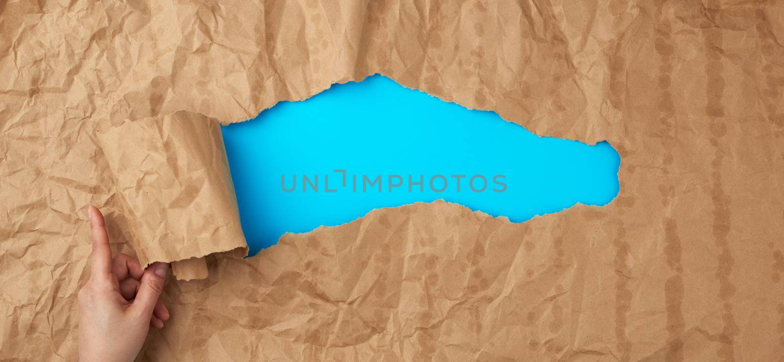 crumpled paper texture from a brown sheet of paper with greasy spots and a large hole with a twisted corner, abstract banner for the designer, blue backdrop. Vintage template with brown paper hole  
