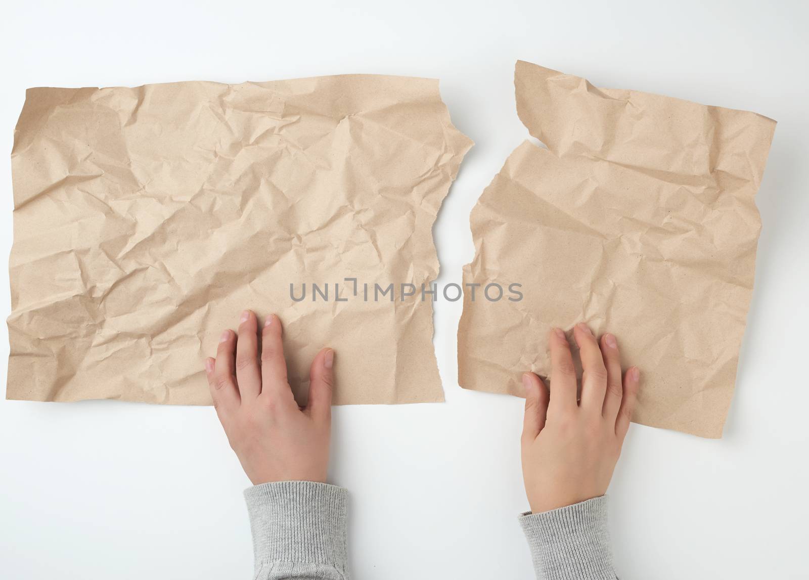 two hands tearing a sheet of brown craft paper, top view