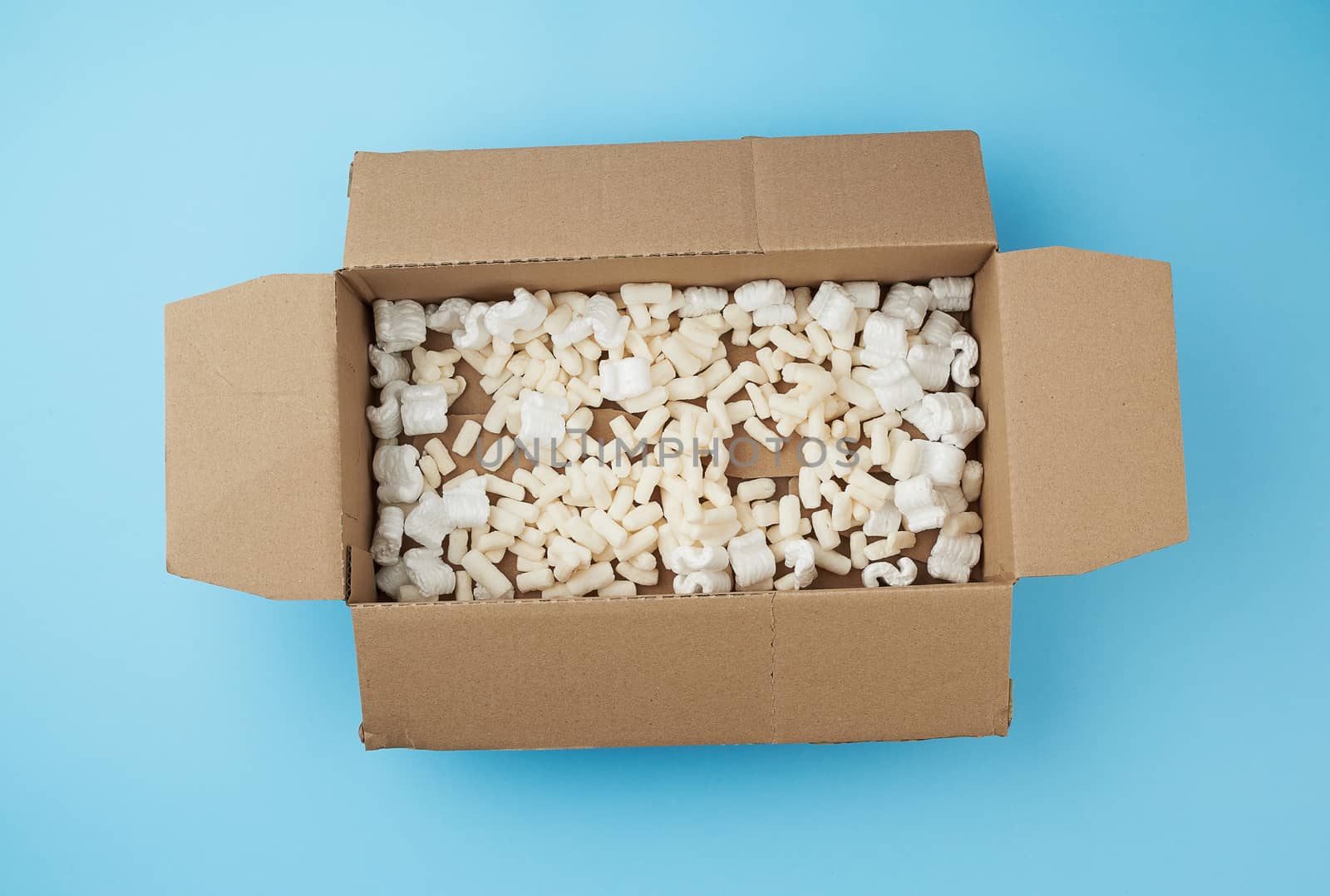 open rectangular brown cardboard box with white foam filling for transporting goods on a blue background, top view