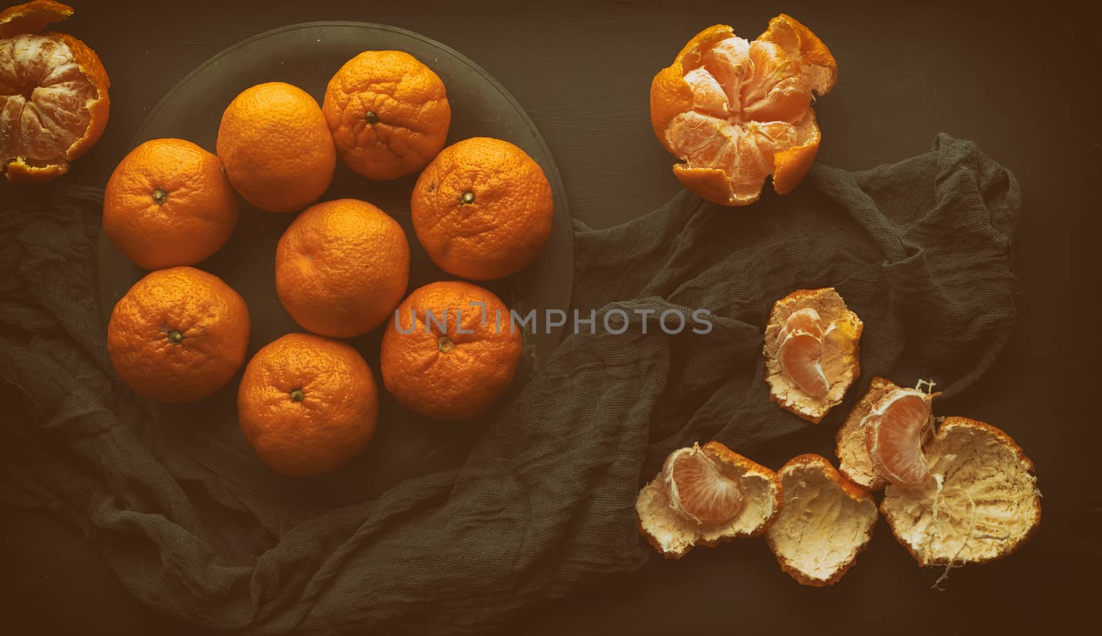 round ripe tangerines in a plate on a black textile napkin, top view, low key