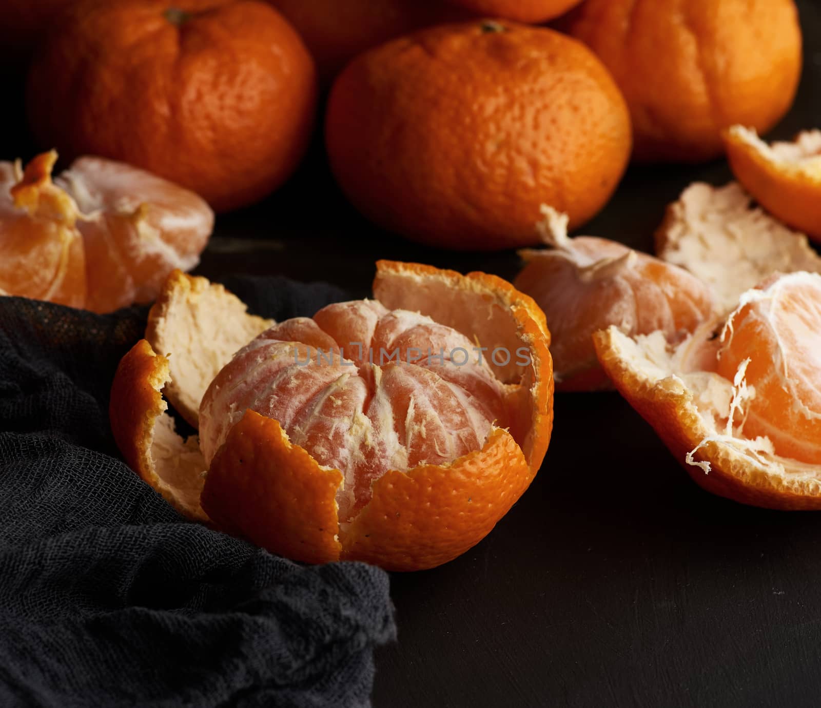 peeled round ripe tangerines in a plate on a black textile napkin, low key