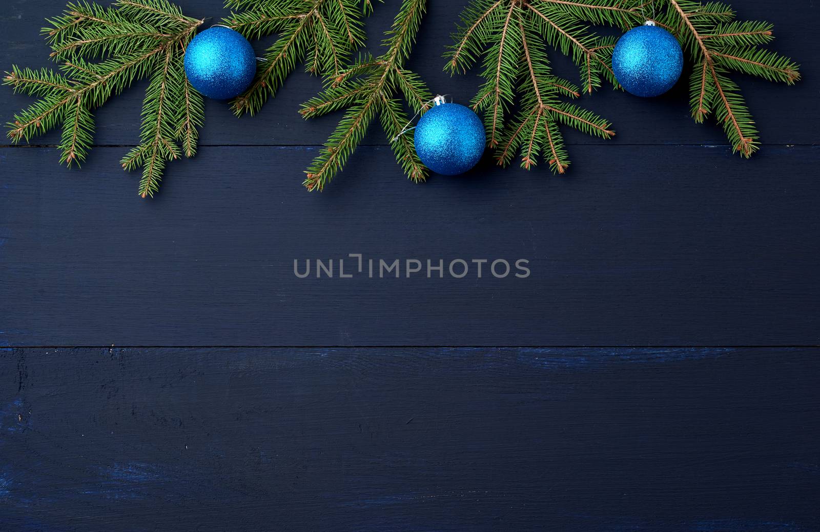 green spruce branches and dark blue shiny Christmas balls on a blue wooden background from boards, festive backdrop for Christmas and New Year, place for an inscription