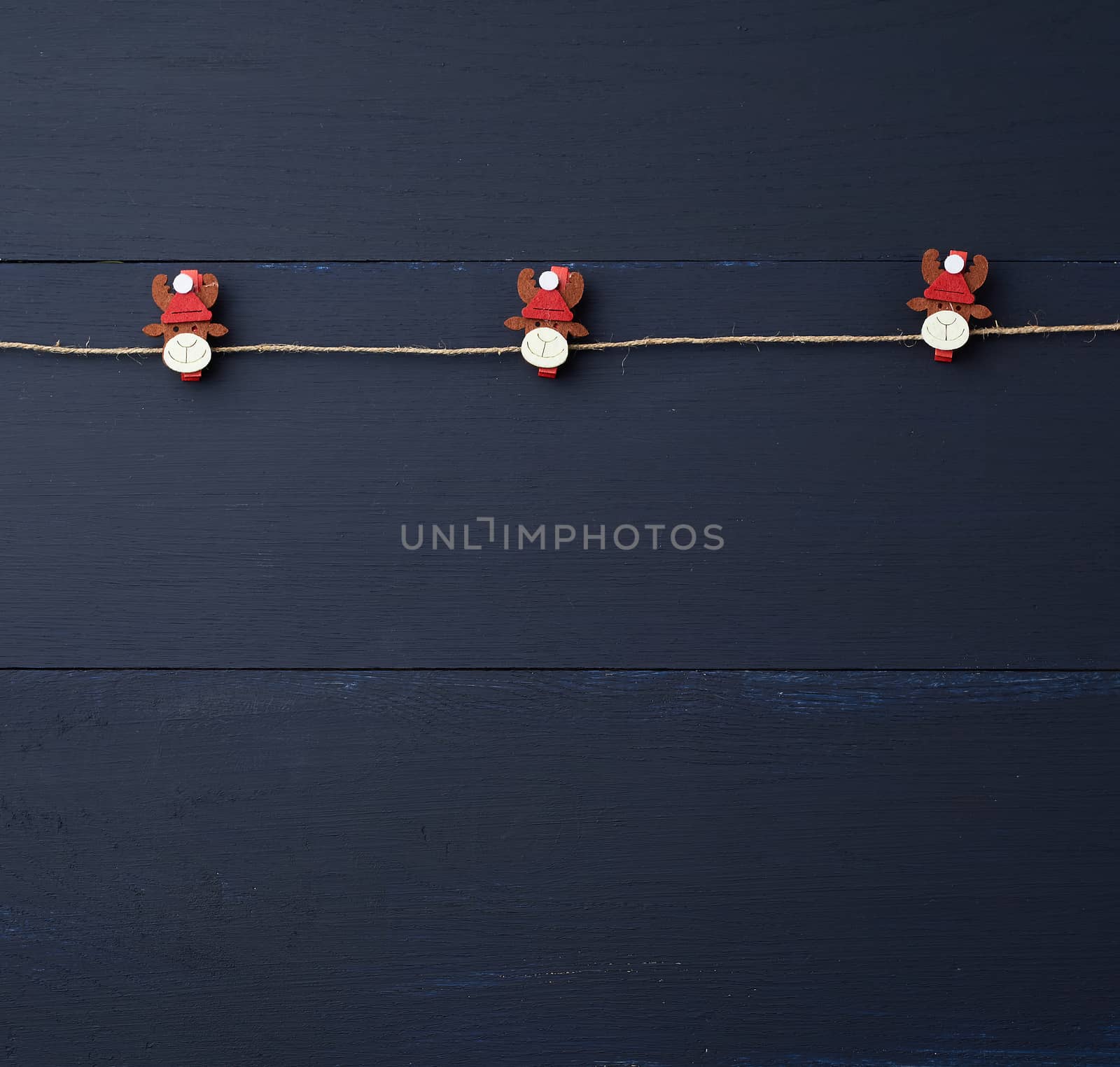 decorative holiday clothespins with a figure of a deer hang on a brown rope, blue wooden background