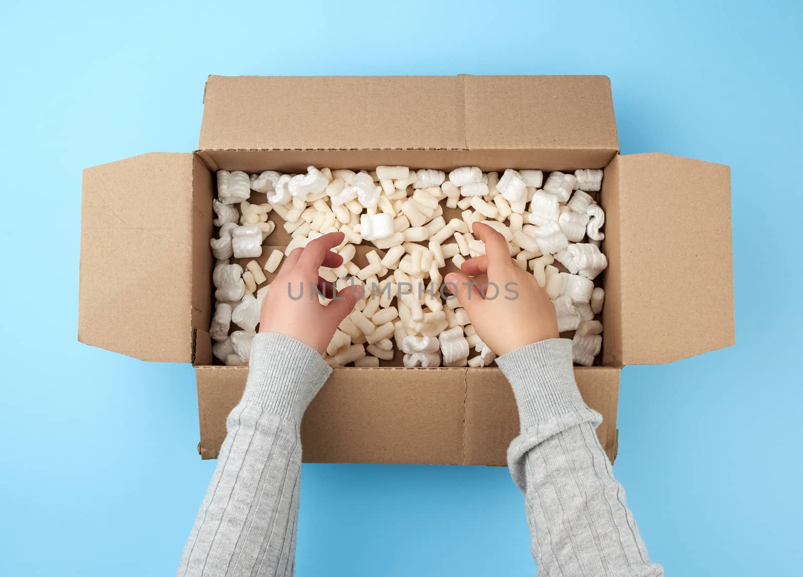 two female hands hold an empty open box of brown cardboard, at the bottom there is a white foam for packaging, top view