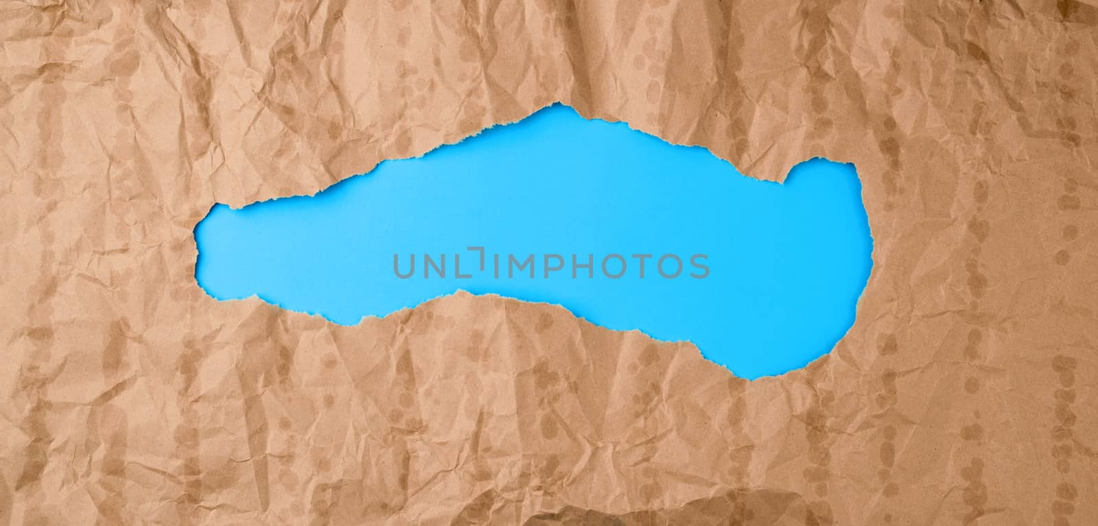 crumpled paper texture from a brown sheet of paper with greasy spots and a large hole. abstract banner for the designer, blue backdrop. 