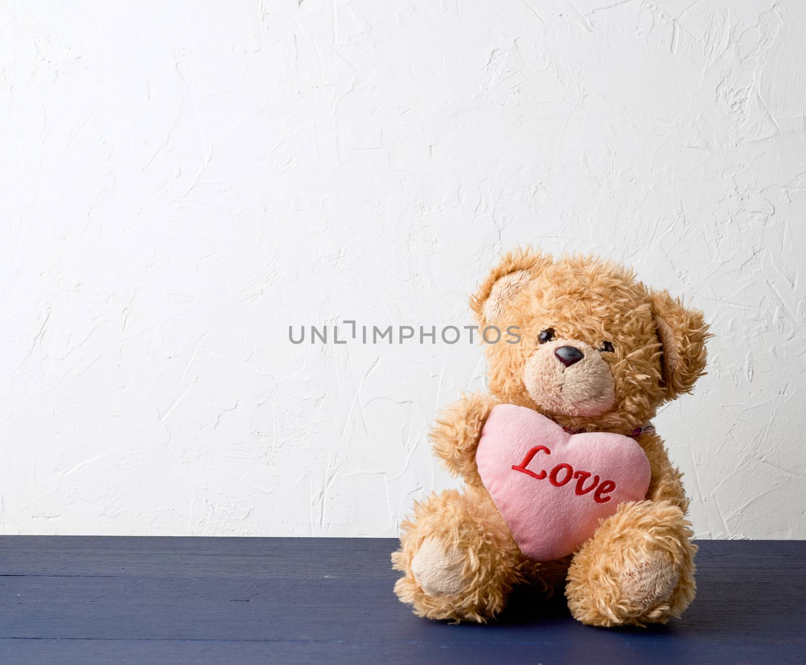 cute brown teddy bear holding a big pink heart and sits on a wooden background, holiday gift for Valentine's Day, copy space