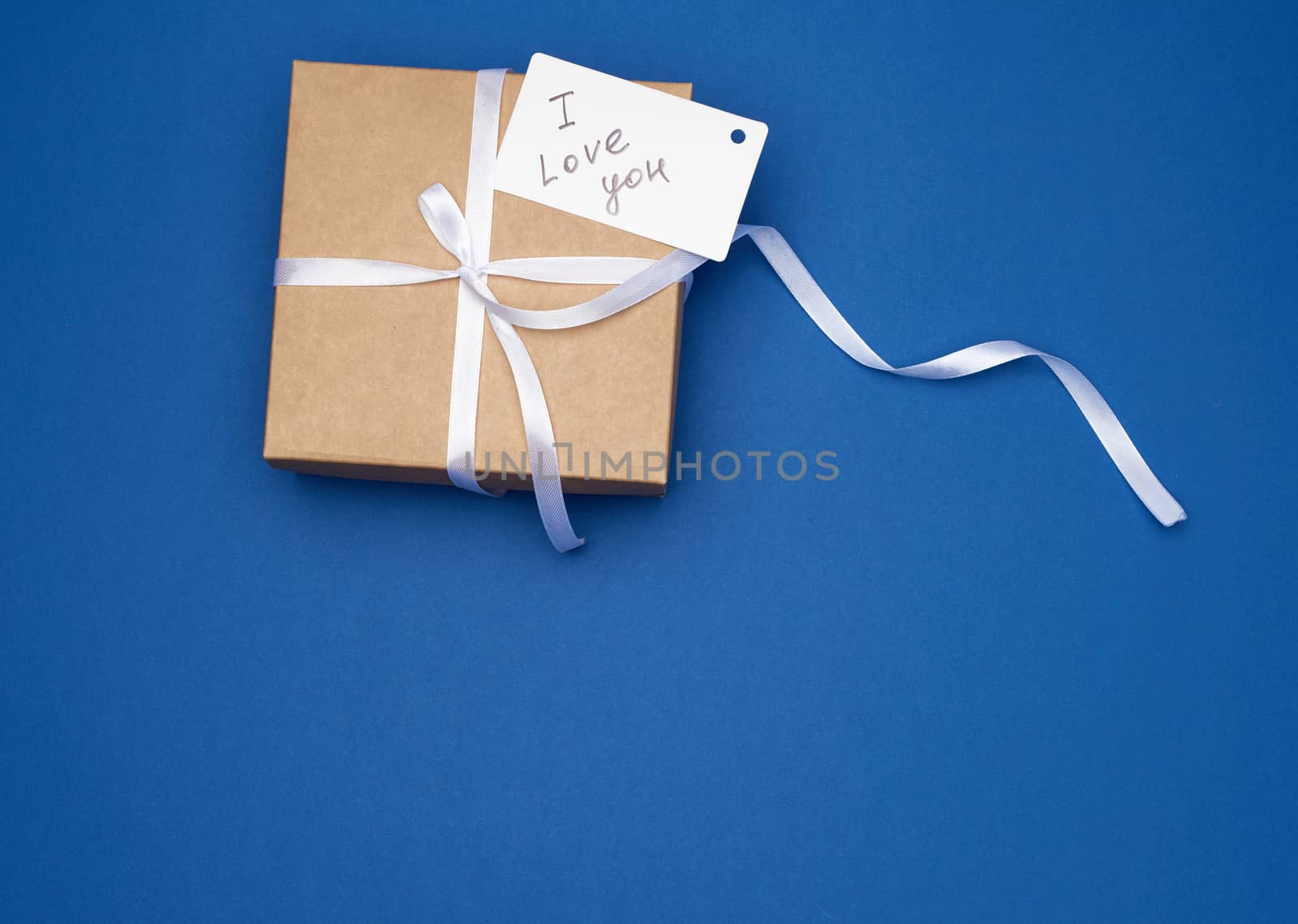 brown gift box with white bow and white paper business card with the inscription i love you, blue background