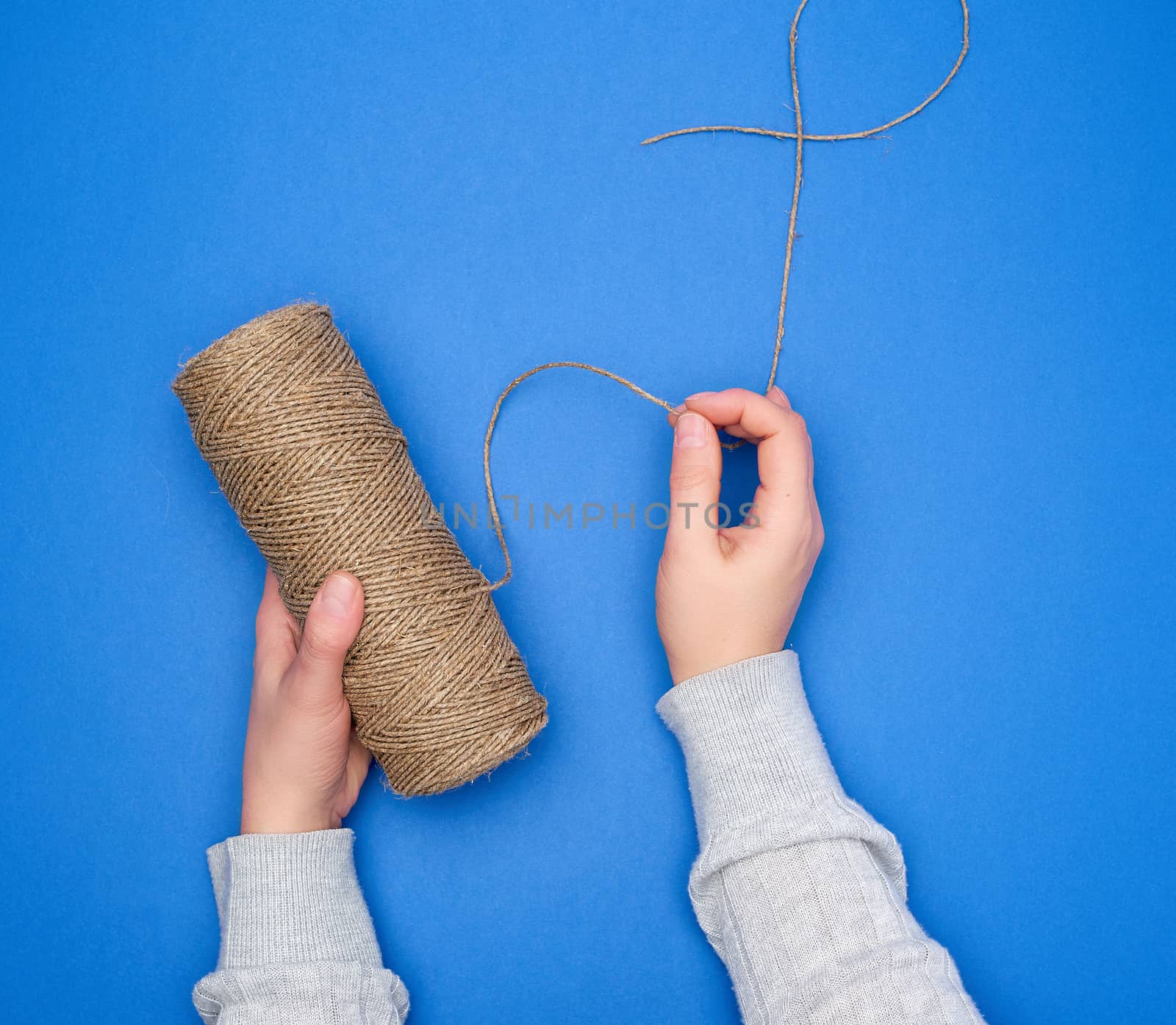 female hands holding a skein with brown eco thread on a blue background, top view