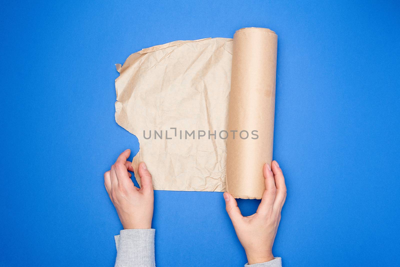 two hands holding a roll of brown parchment paper on a blue background, top view