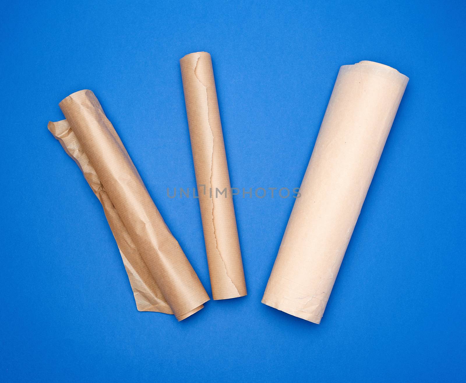 three rolled rolls with brown parchment baking paper on a blue background, top view