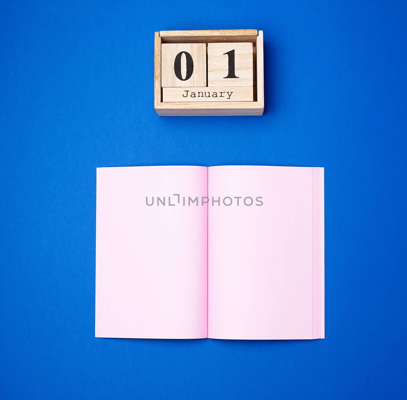wooden retro calendar with the date of January 1 and an open notebook with empty pink sheets, concept of the beginning of the year and new plans for the future