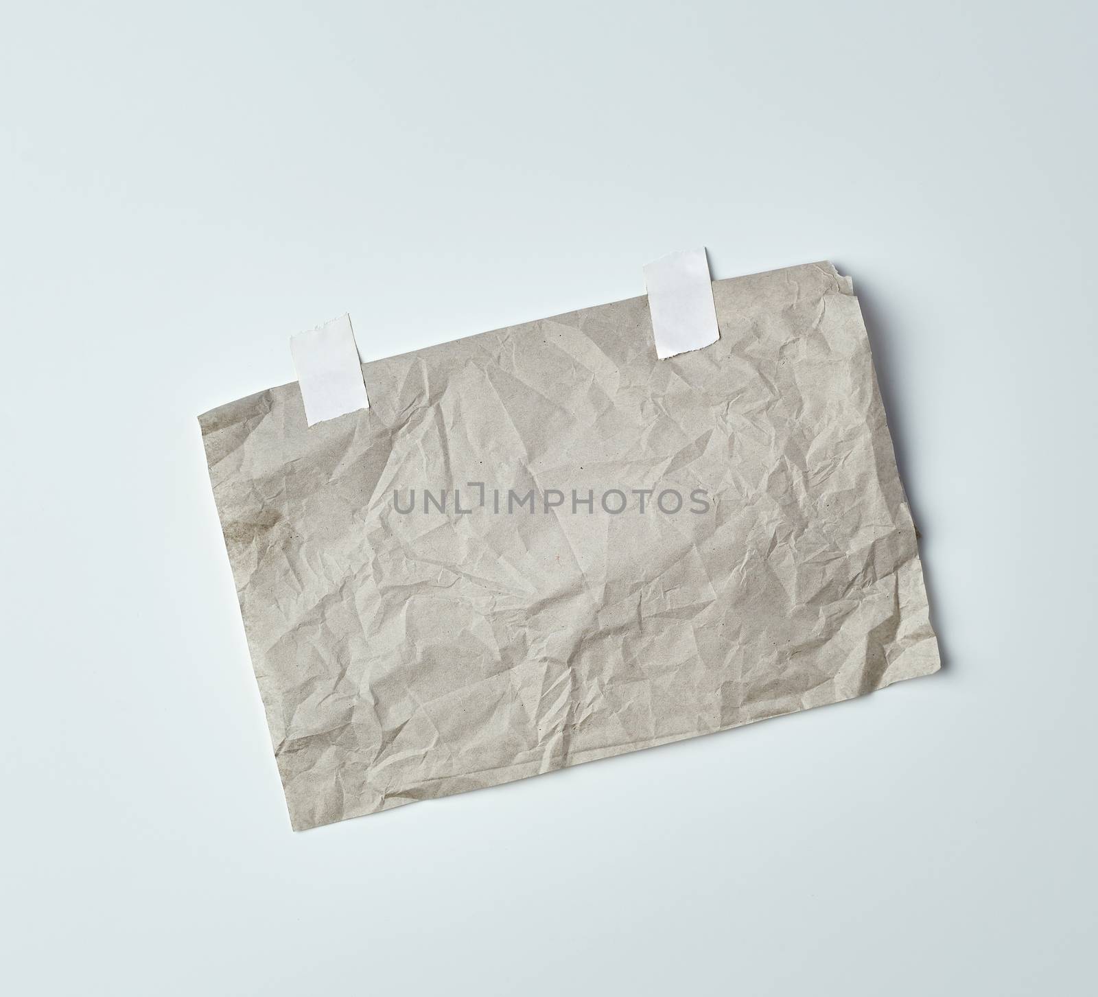 gray crumpled sheet of paper glued with white adhesive tape on a white background, place for text