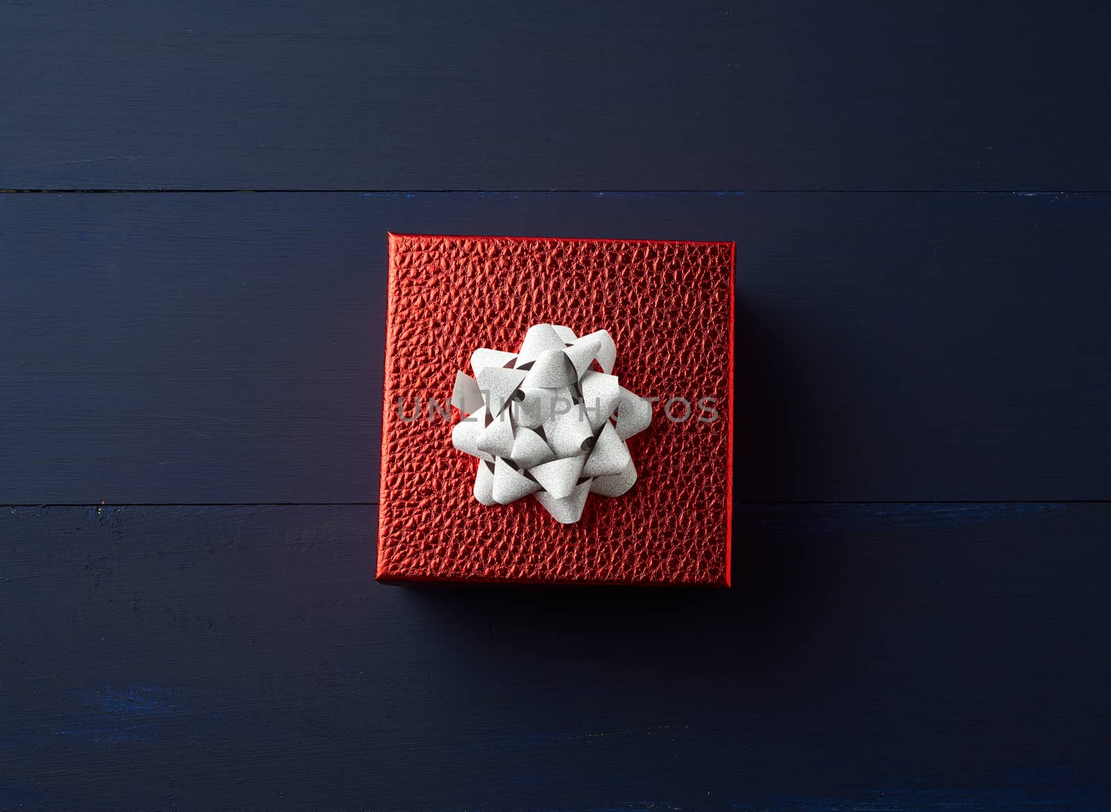 square red box tied with a golden ribbon, concept of congratulations and gifts, top view, blue wooden background