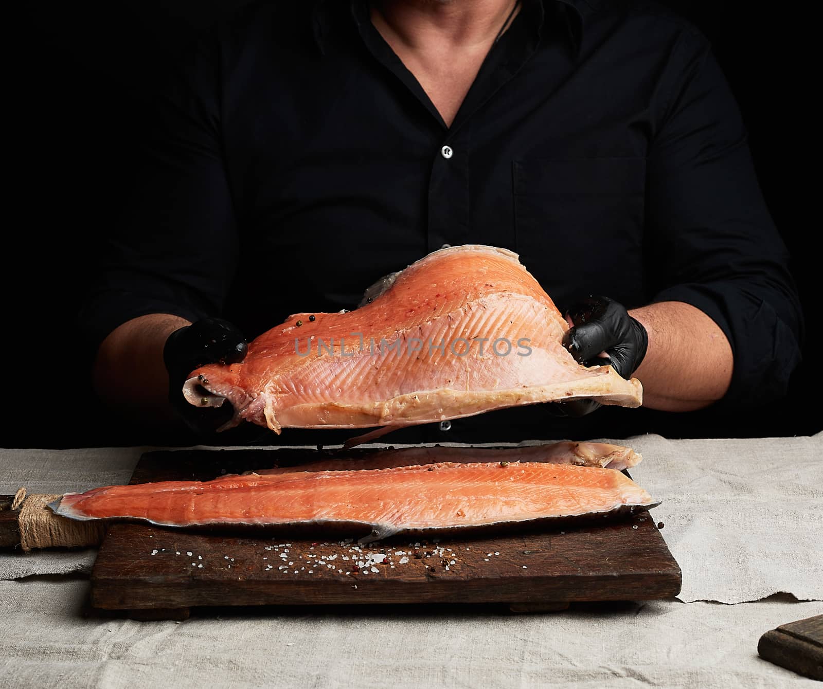 chef in a black shirt and black latex gloves holds a large piece of salmon fish fillet over the table, cooking process, clouse up