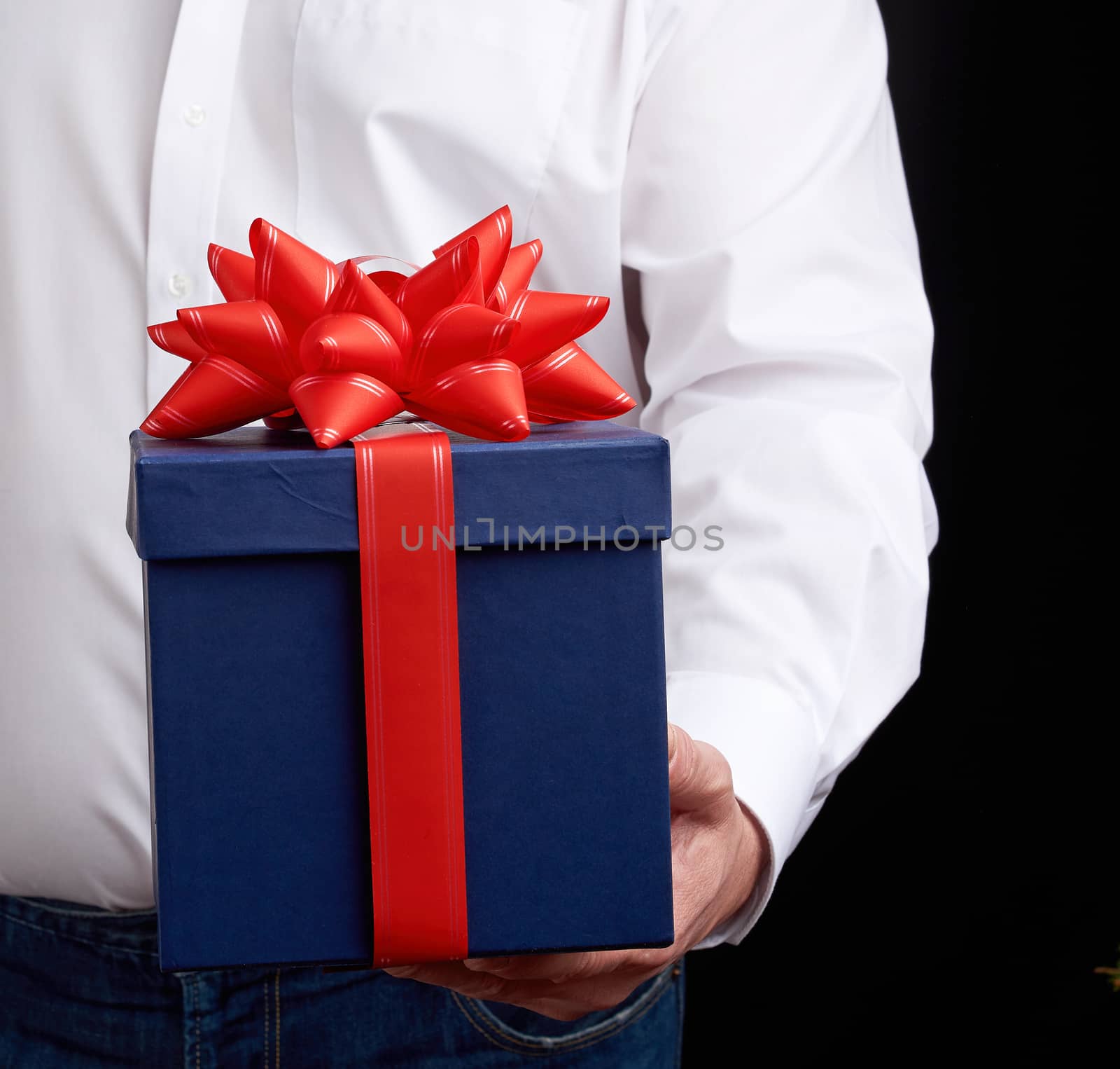 man in a white shirt holds a blue gift cardboard box with a red bow, concept of a congratulation on the holiday, anniversary, surprise