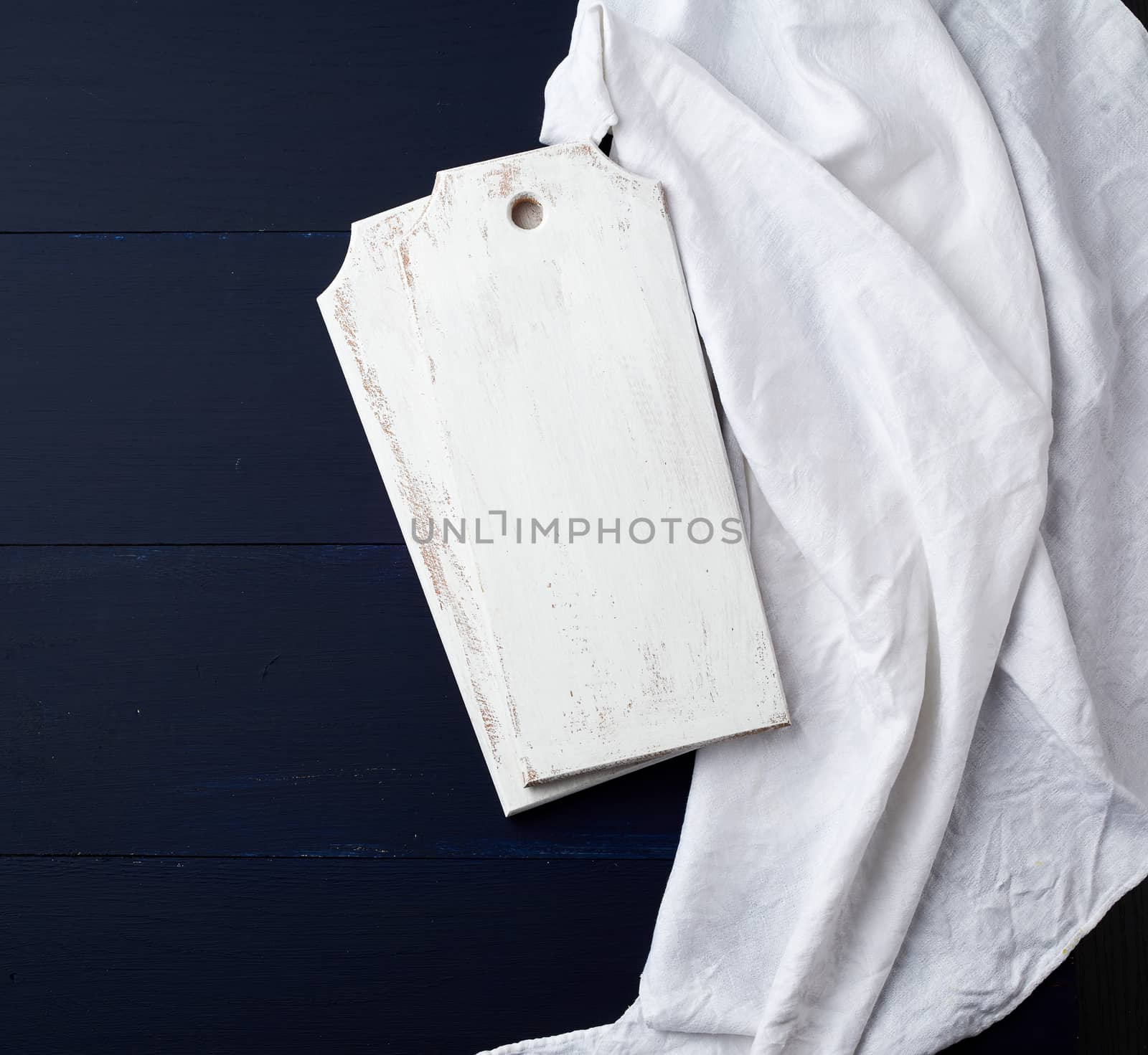 two rectangular white cutting kitchen boards on a blue wooden background, next to a white textile towel, top view. Copy space