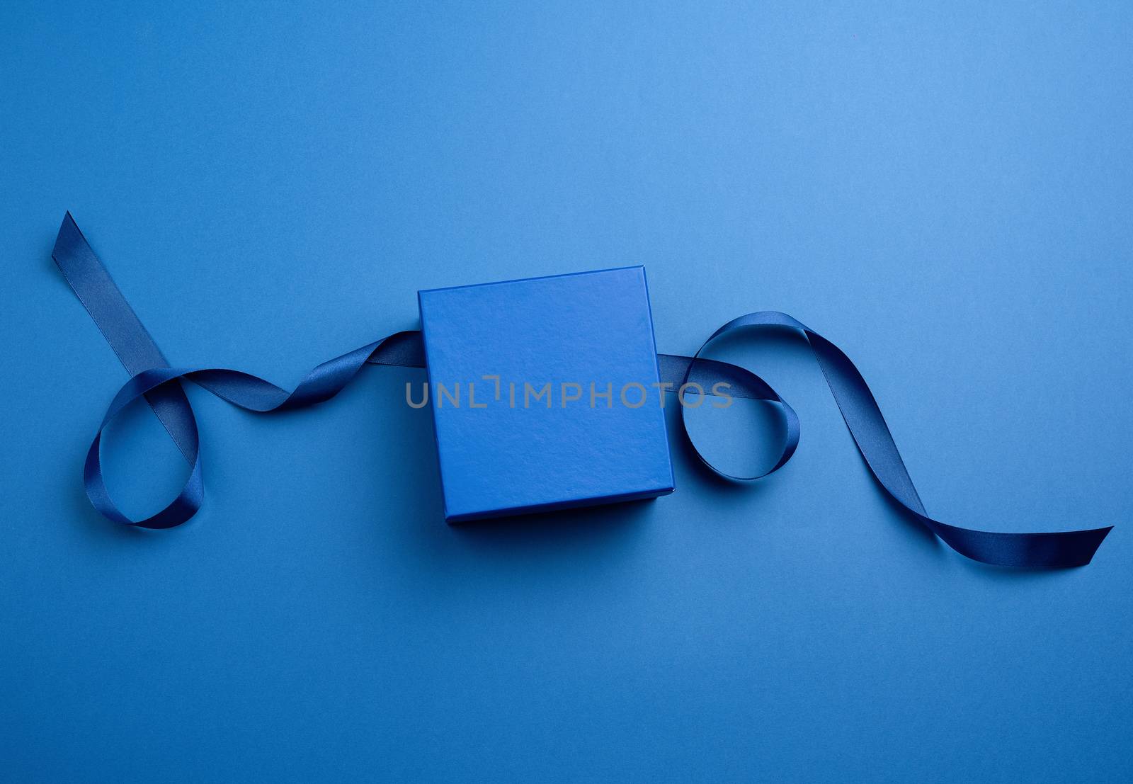 closed cardboard gift square box, ribbons for packaging on a dark blue background, top view, trend colors