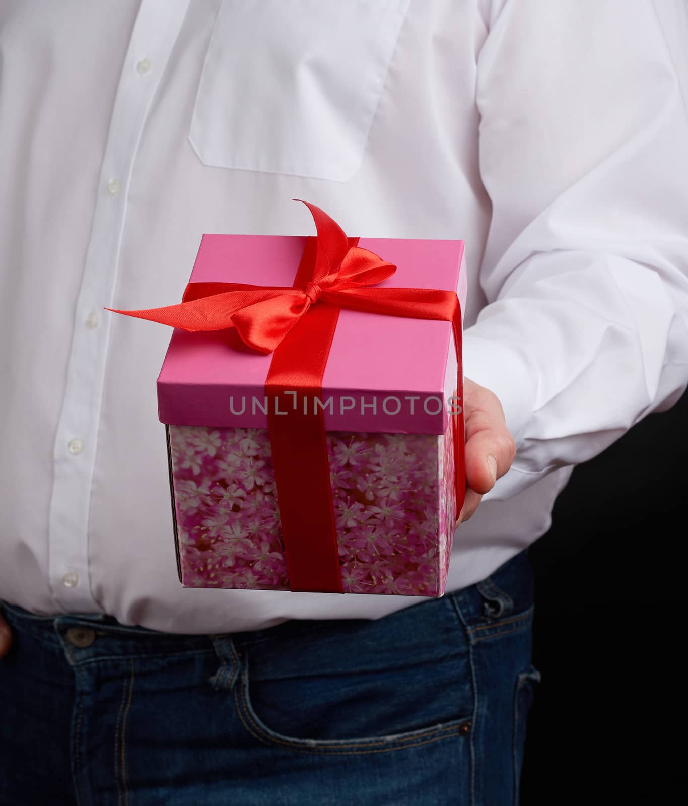 adult man in a white shirt holds a pink gift cardboard box with a bow, concept of a congratulation on the holiday, anniversary, surprise