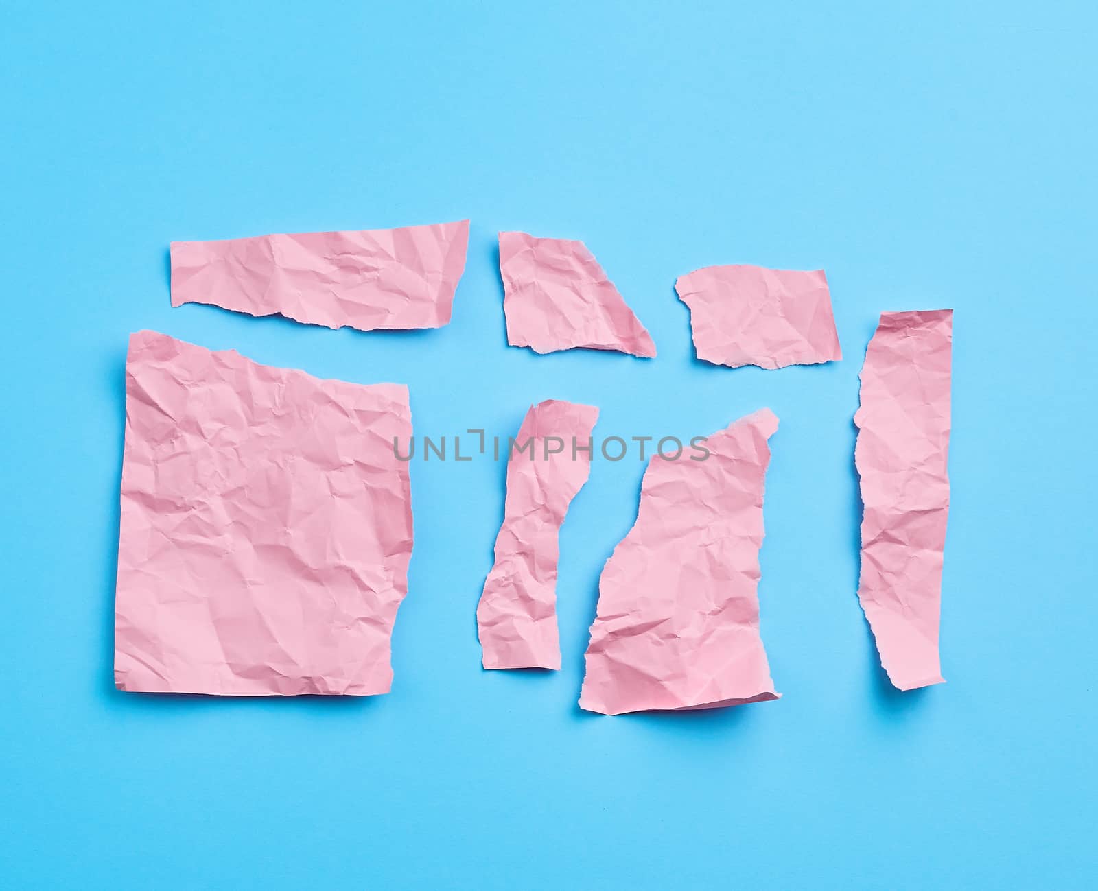 set of various cut pieces of pink crumpled paper on a blue background, close up