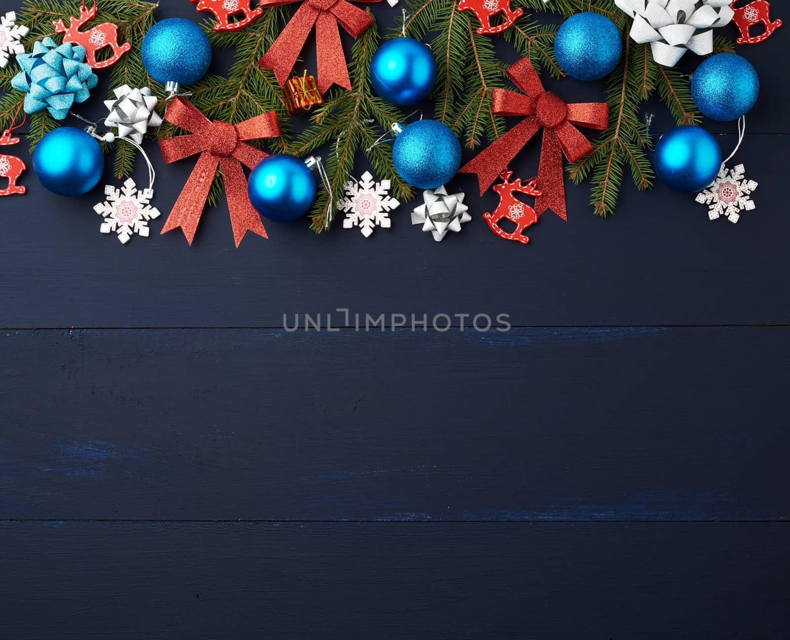 green spruce branches, Christmas blue and pink balls, red shiny bows and carved wooden decor on a blue wooden background from boards