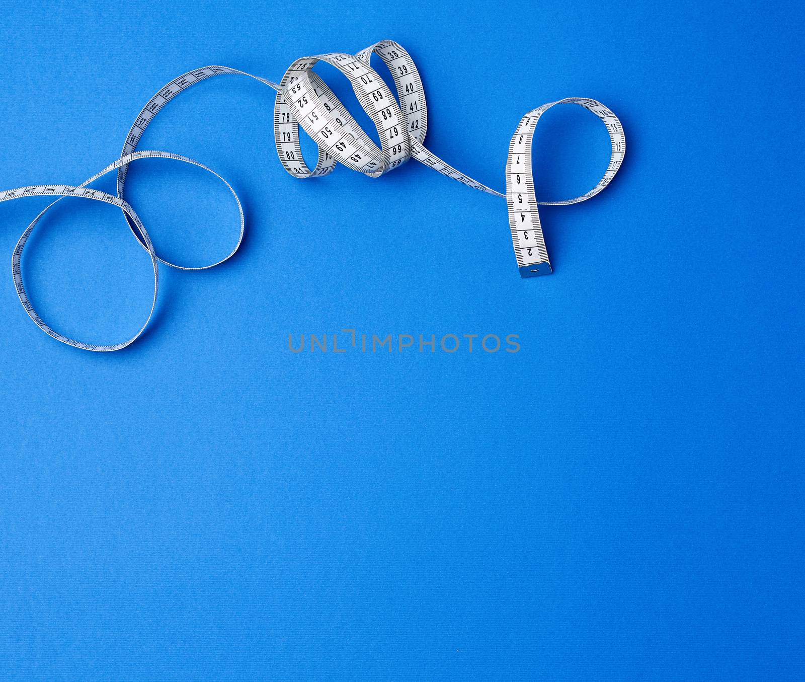 twisted white measuring tape on a blue background, copy space. Weight loss concept. Fitness background. 