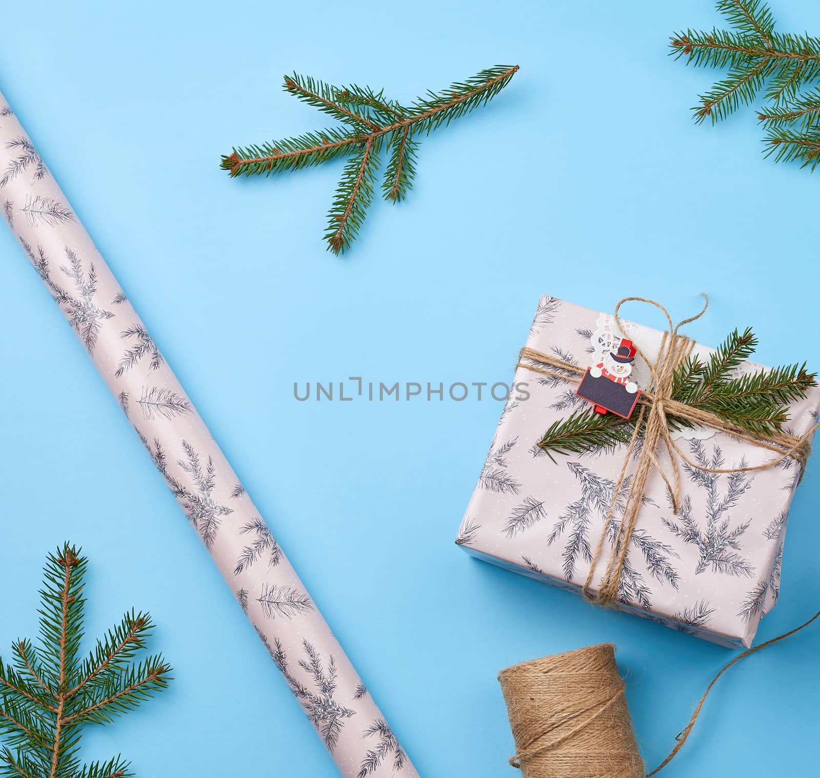 gift wrapped in pink paper and tied with a brown rope, decor from a green spruce branch on a blue background, top view