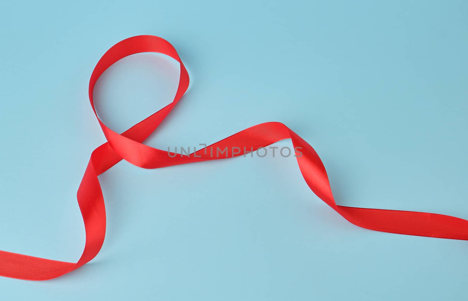 red silk thin ribbon twisted on a blue background, trendy classic color, close up