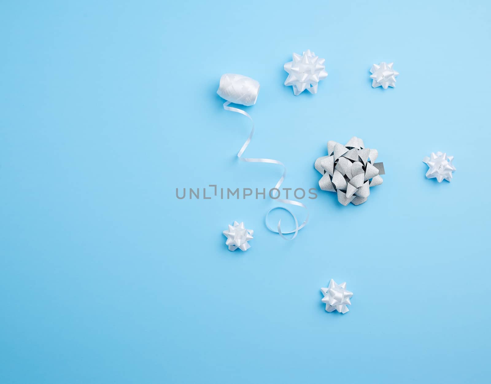 knitted white bows and white ribbon on a blue background, decor for decorating gifts, top view