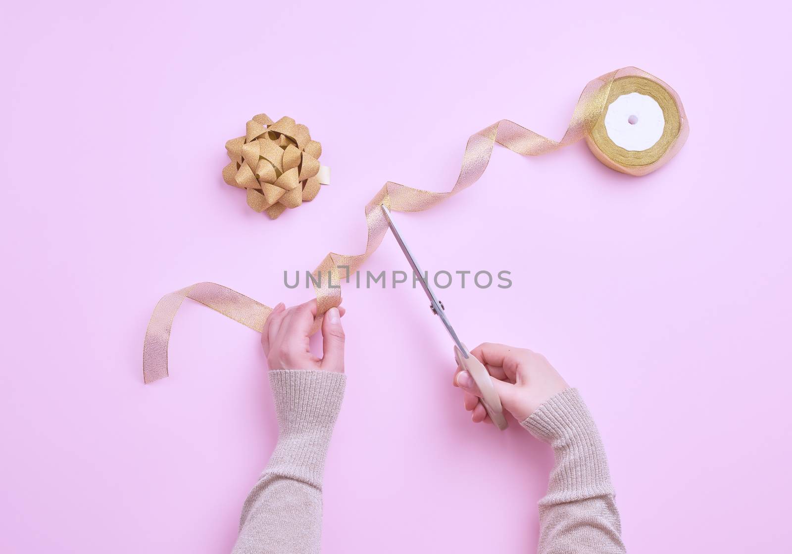 female hands cut golden ribbons in a roll for packing gifts, pink background, top view