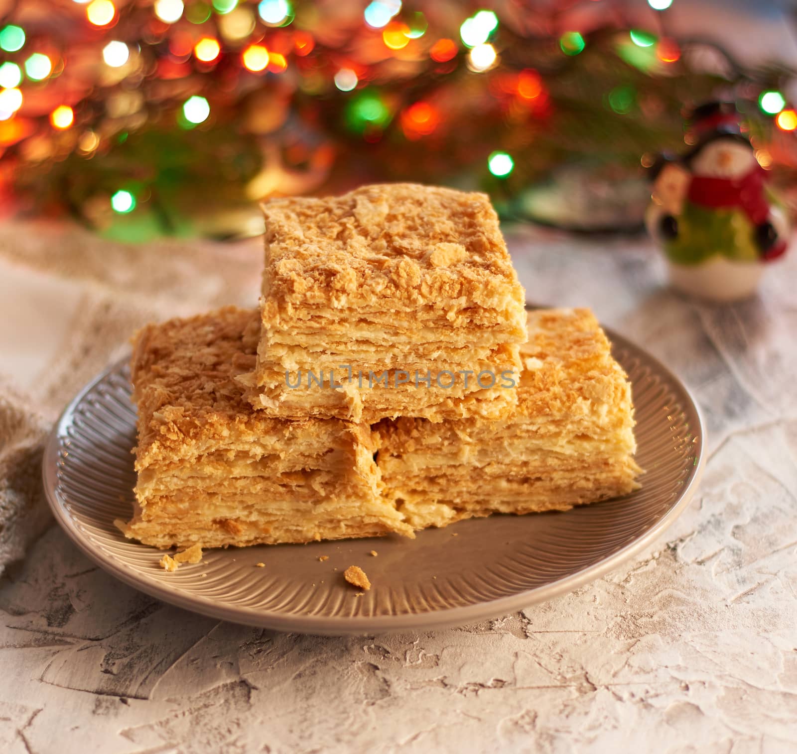 stack of slices of Napoleon cake made of puff pastry and butter cream in a gray ceramic plate, behind burning garlands