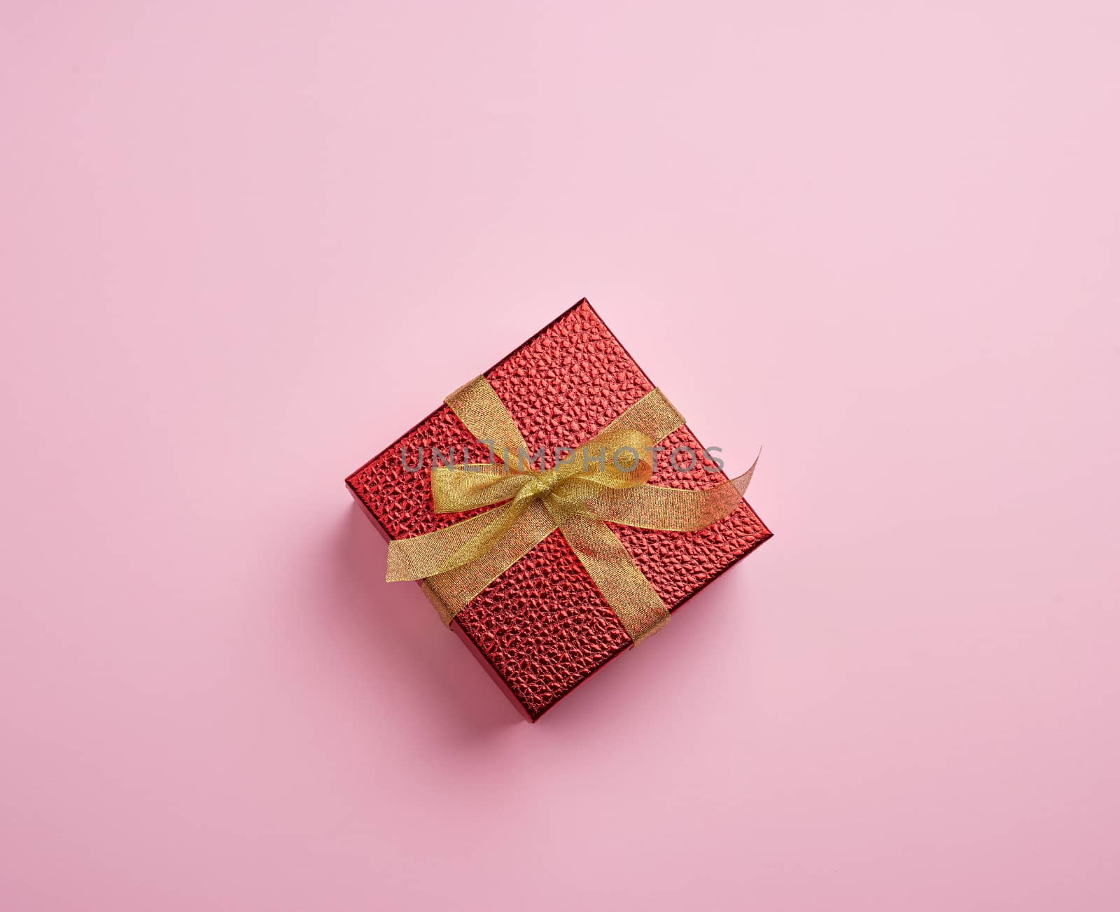 square red box tied with a golden ribbon, concept of congratulations and gifts, top view, pink background