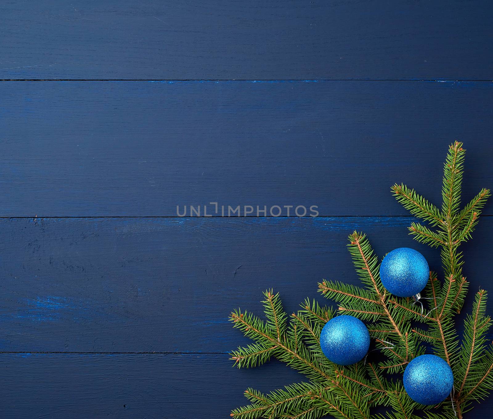 green spruce branches and dark blue shiny Christmas balls on a blue wooden background from boards, festive backdrop for Christmas and New Year, place for an inscription