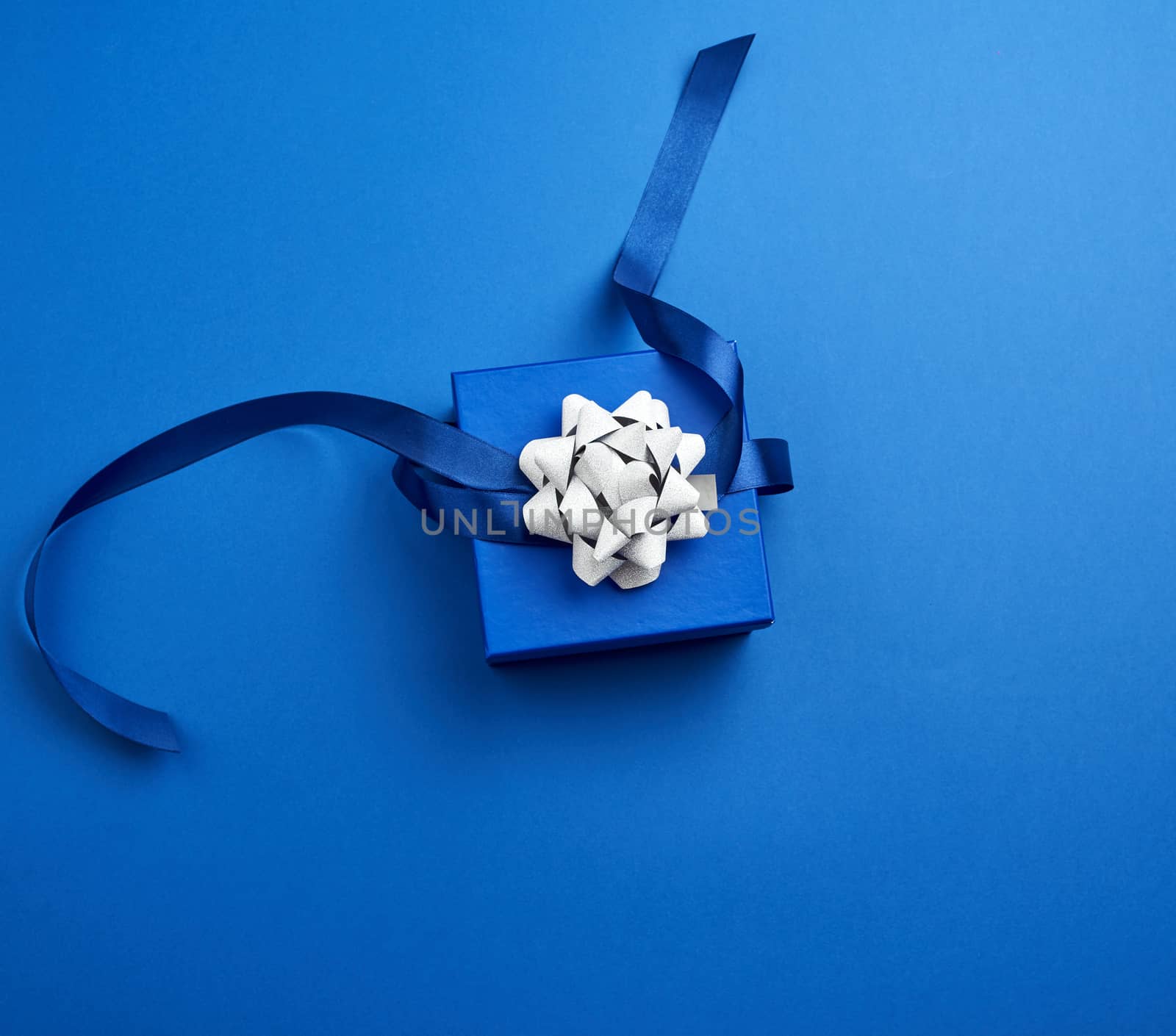 closed square blue box with a gift tied with a blue ribbon with a bow on a blue classic background, top view, trend color 