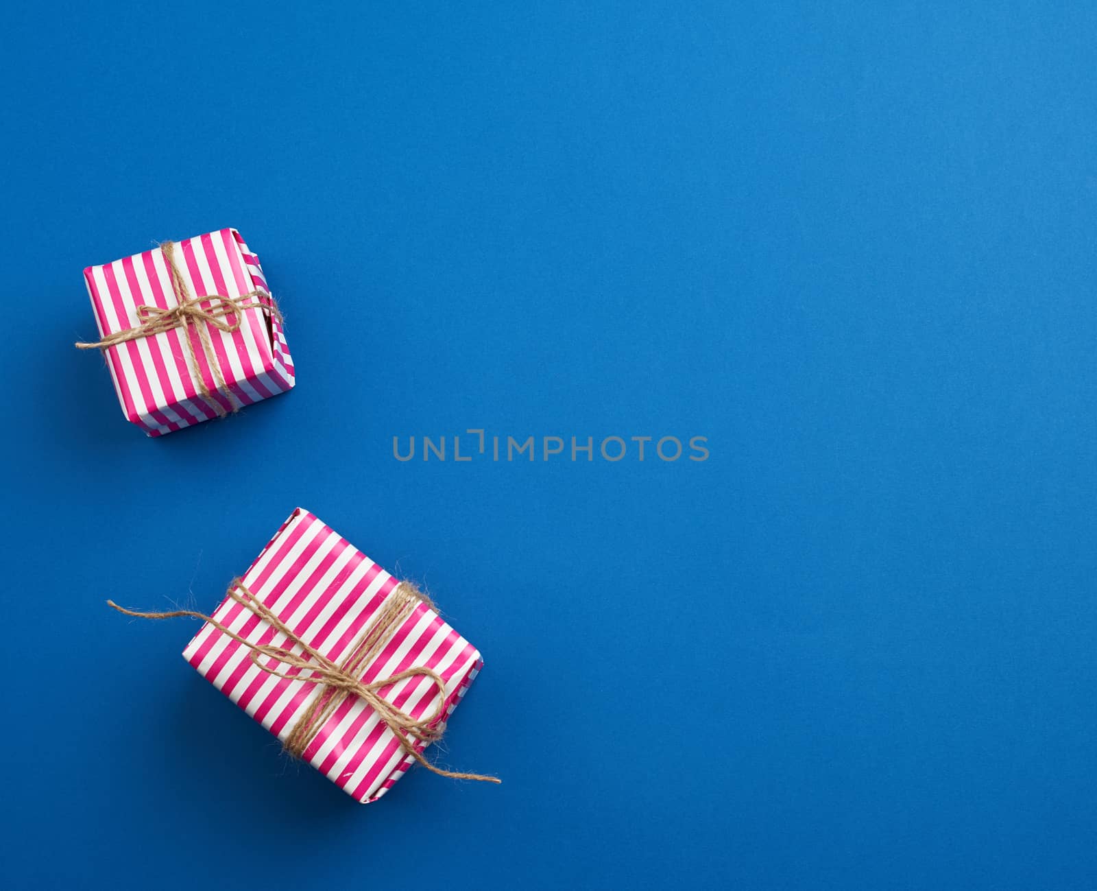 two gifts wrapped in pink striped paper on a blue background, top view, copy space