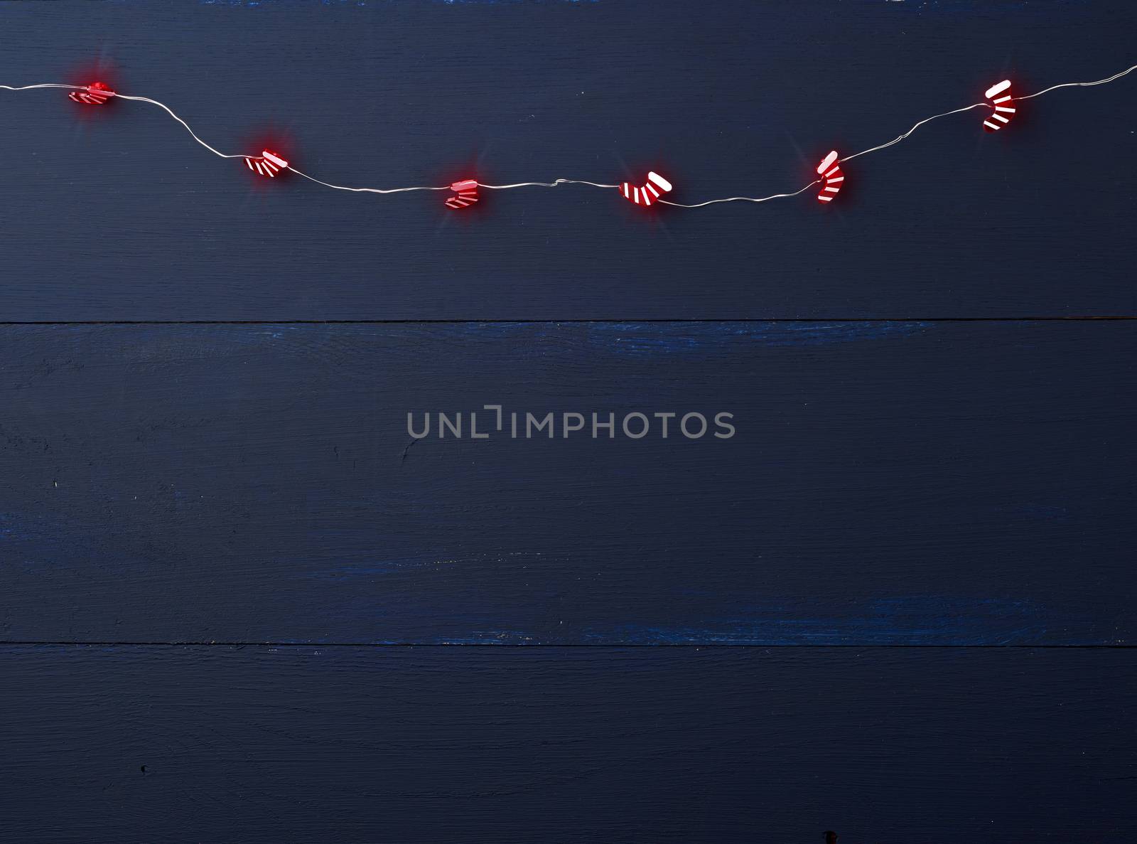 burning christmas garland of small red boots on a blue wooden background from parallel boards, copy space. Festival decor. Christmas garland