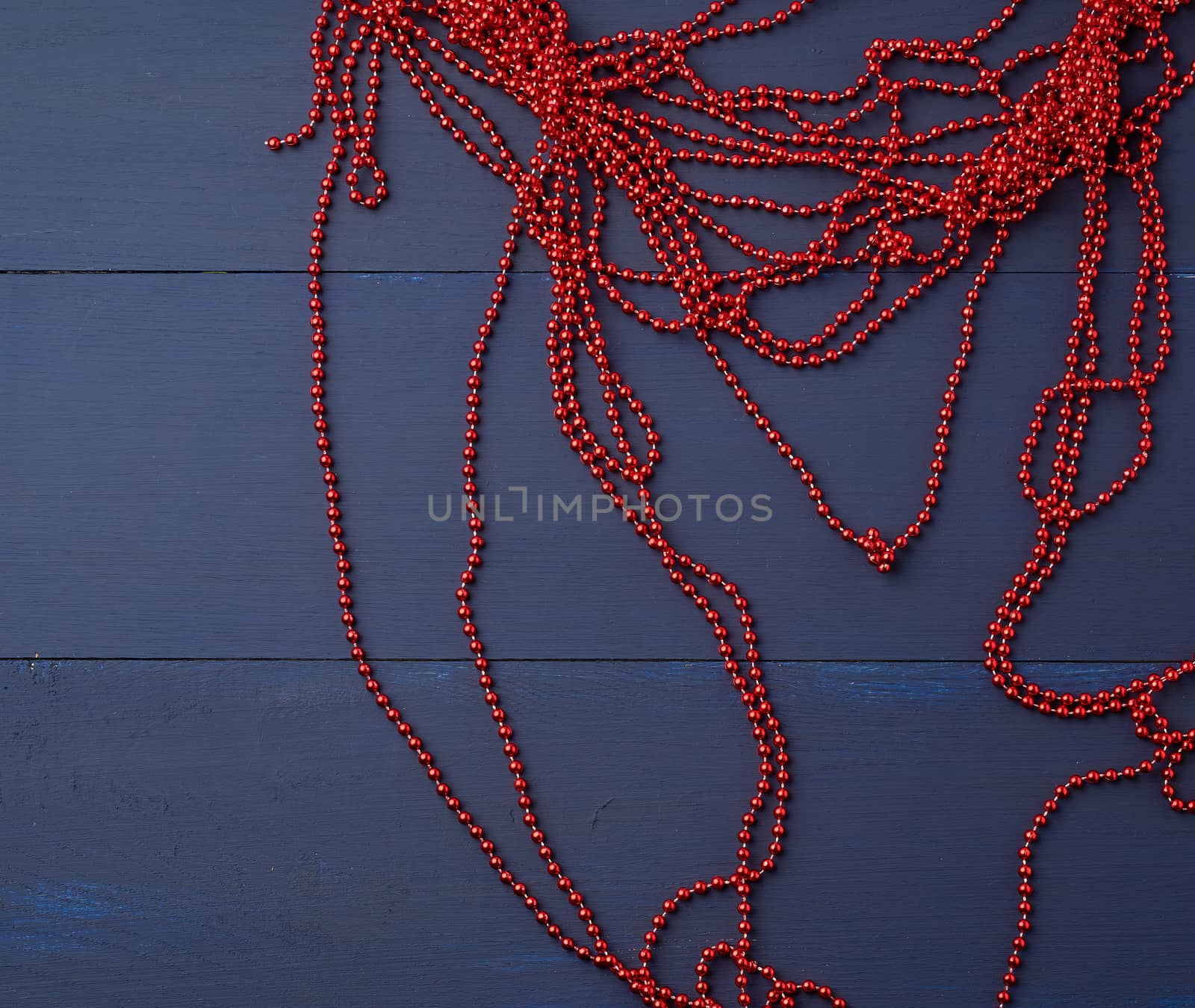 Christmas garland of round red beads strung on a thread, blue wooden background from boards. Elegant holiday frame. Party backdrop. Winter season.