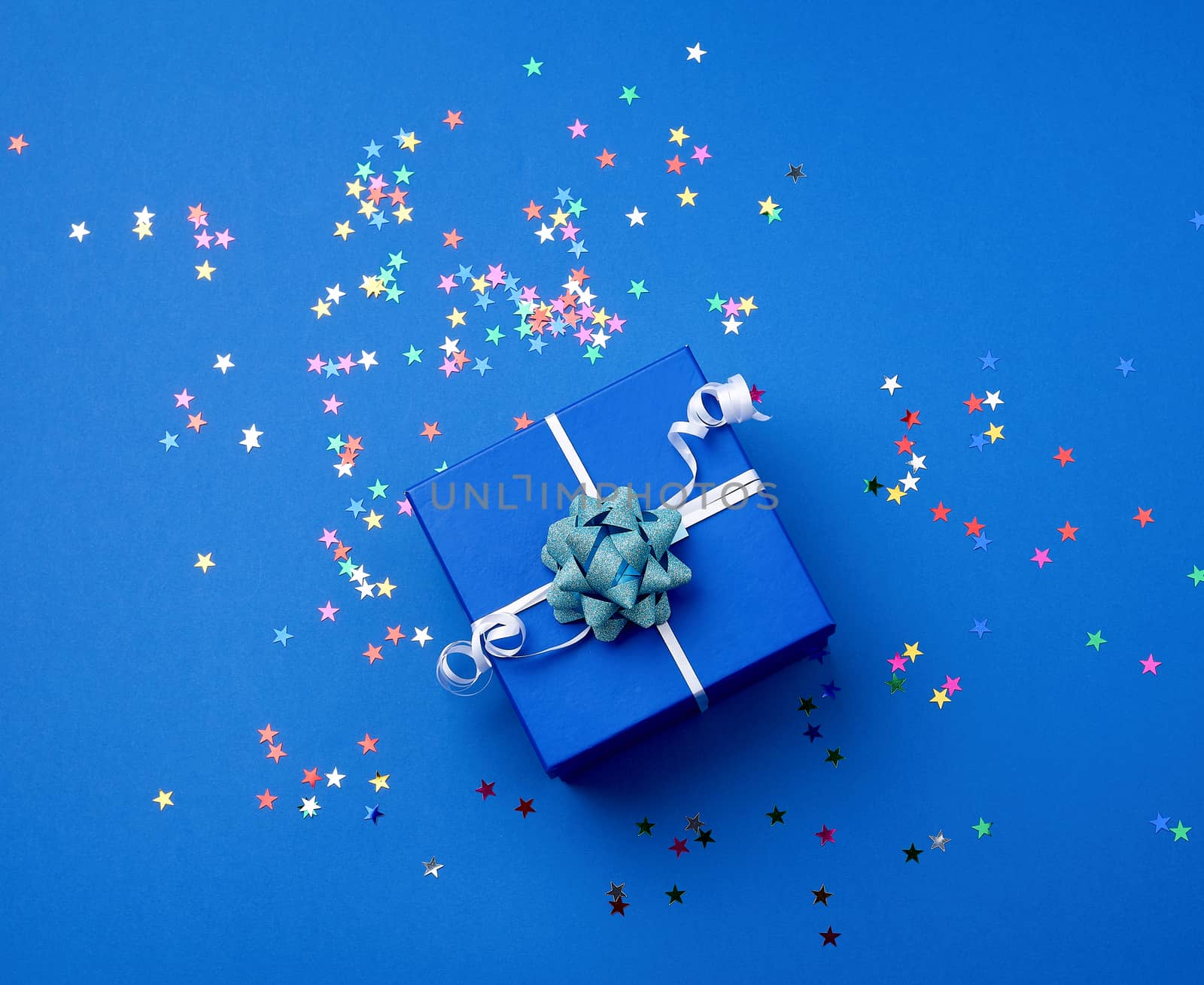 square blue  box with a bow and multicolored sparkles on a blue background, top view. Valentine gift