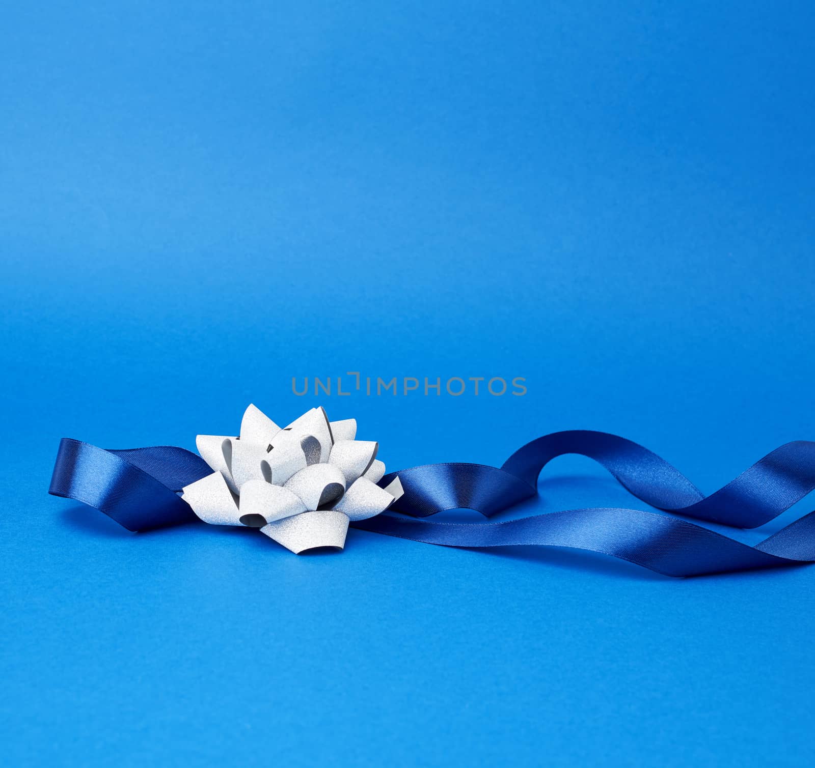 blue silk thin ribbon twisted and gray shiny bow on a blue background, trendy classic color, close up