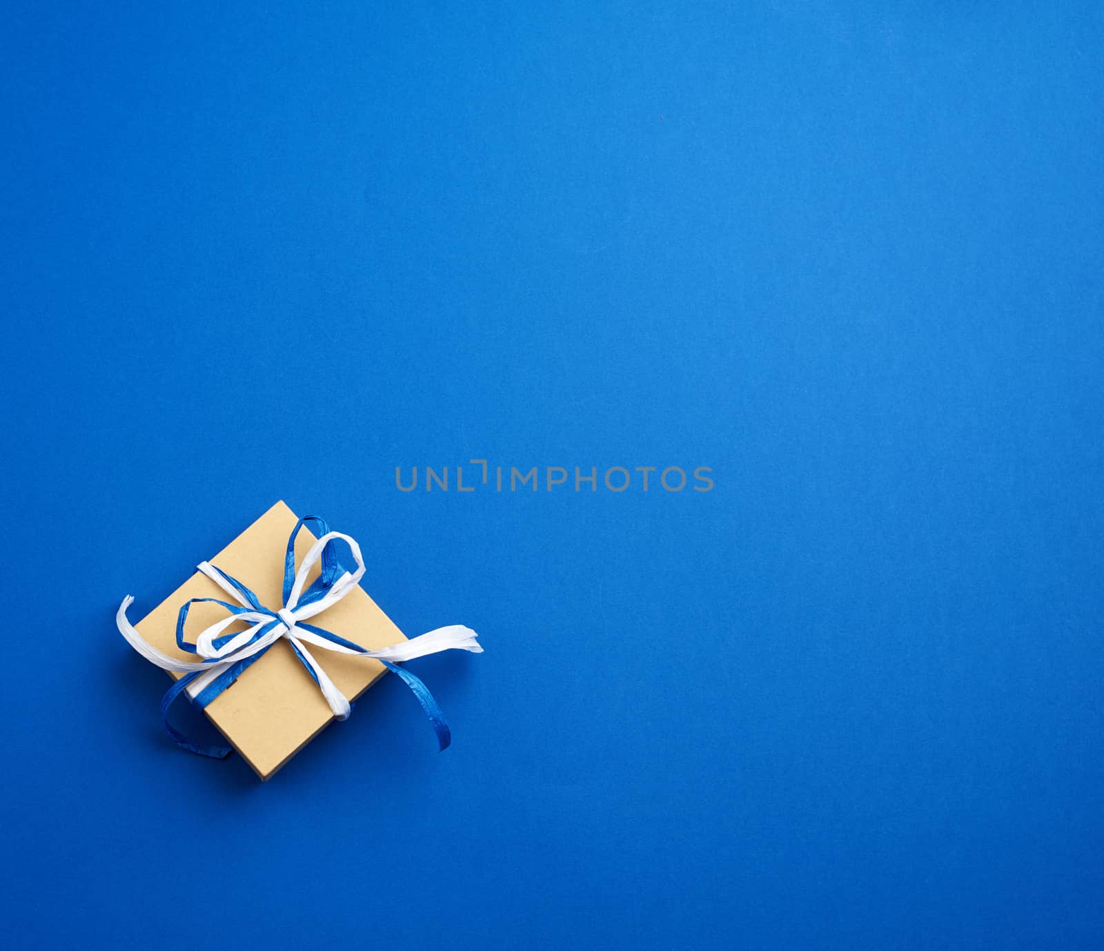 brown cardboard gift square box, bows on a blue background, top view. Festive concept, copy space
