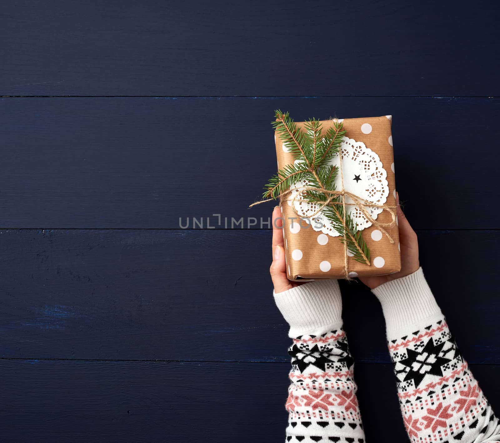 two female hands hold a paper closed box on a blue wooden background. Festive concept