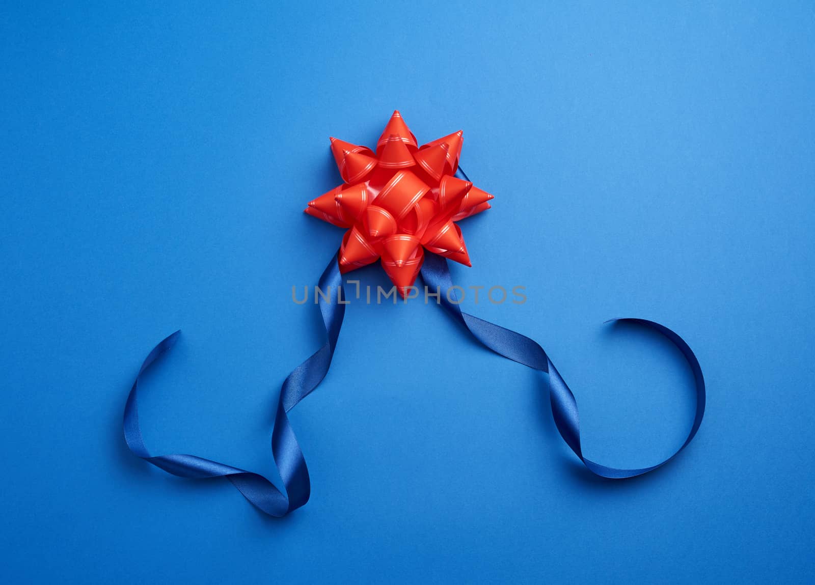 blue silk thin ribbon twisted and red shiny bow on a blue background, trendy classic color, close up