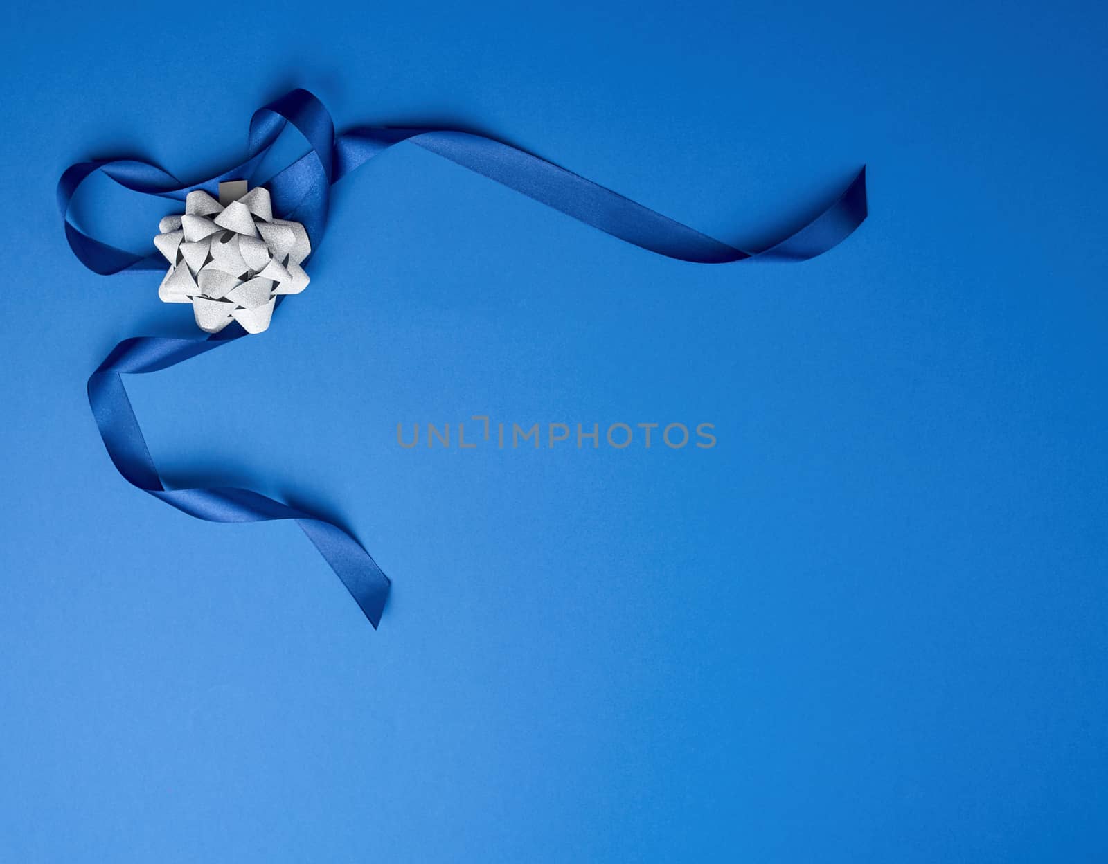 blue silk thin ribbon twisted and gray shiny bow on a blue background, trendy classic color, copy space