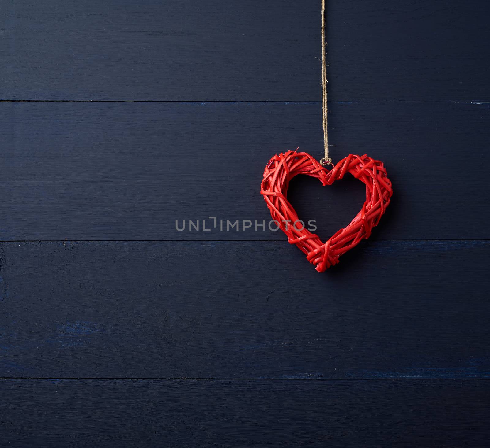 red wicker decorative heart hanging on brown rope, blue wooden festive background for Valentine's day