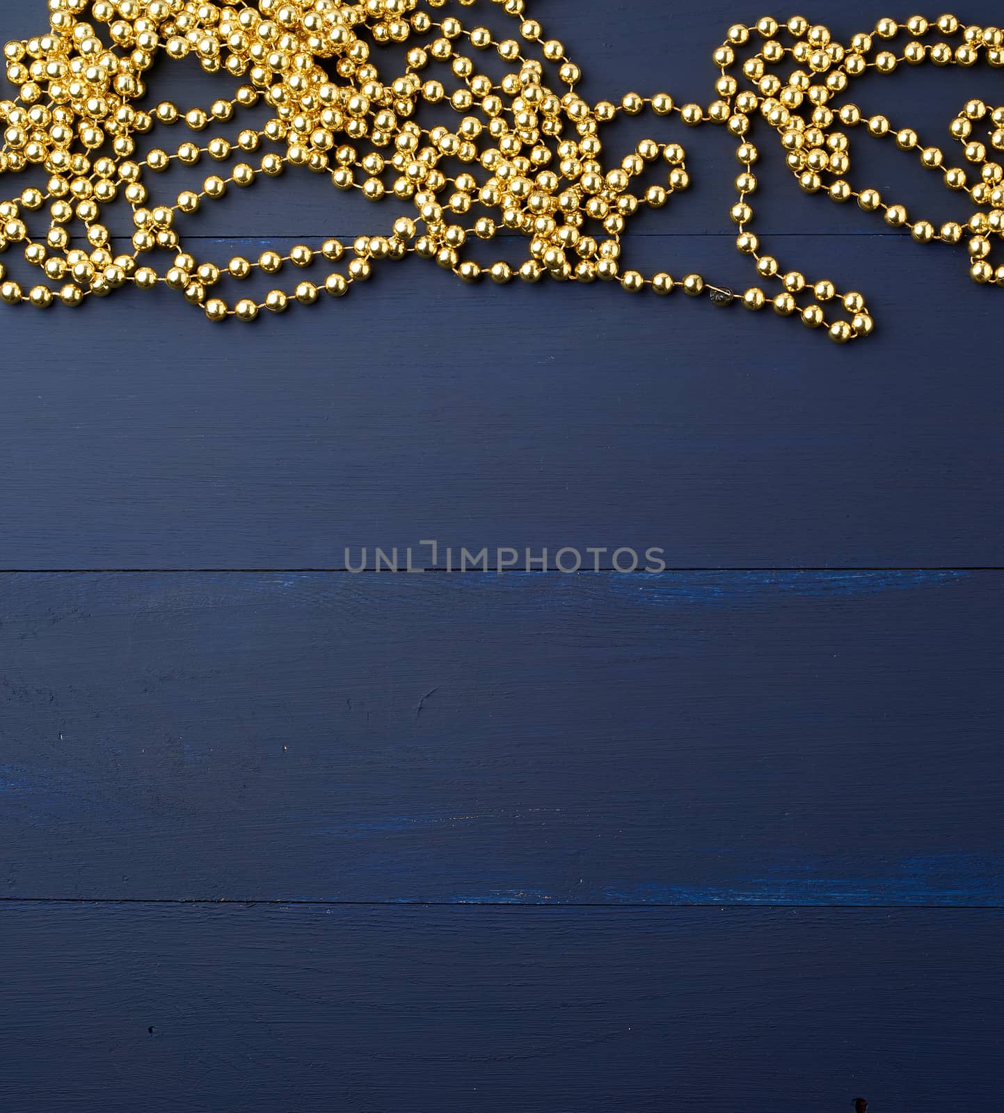 Christmas garland of round golden beads strung on a string, blue wooden background from boards. Golden garland ball christmas shine in beautiful style, copy space