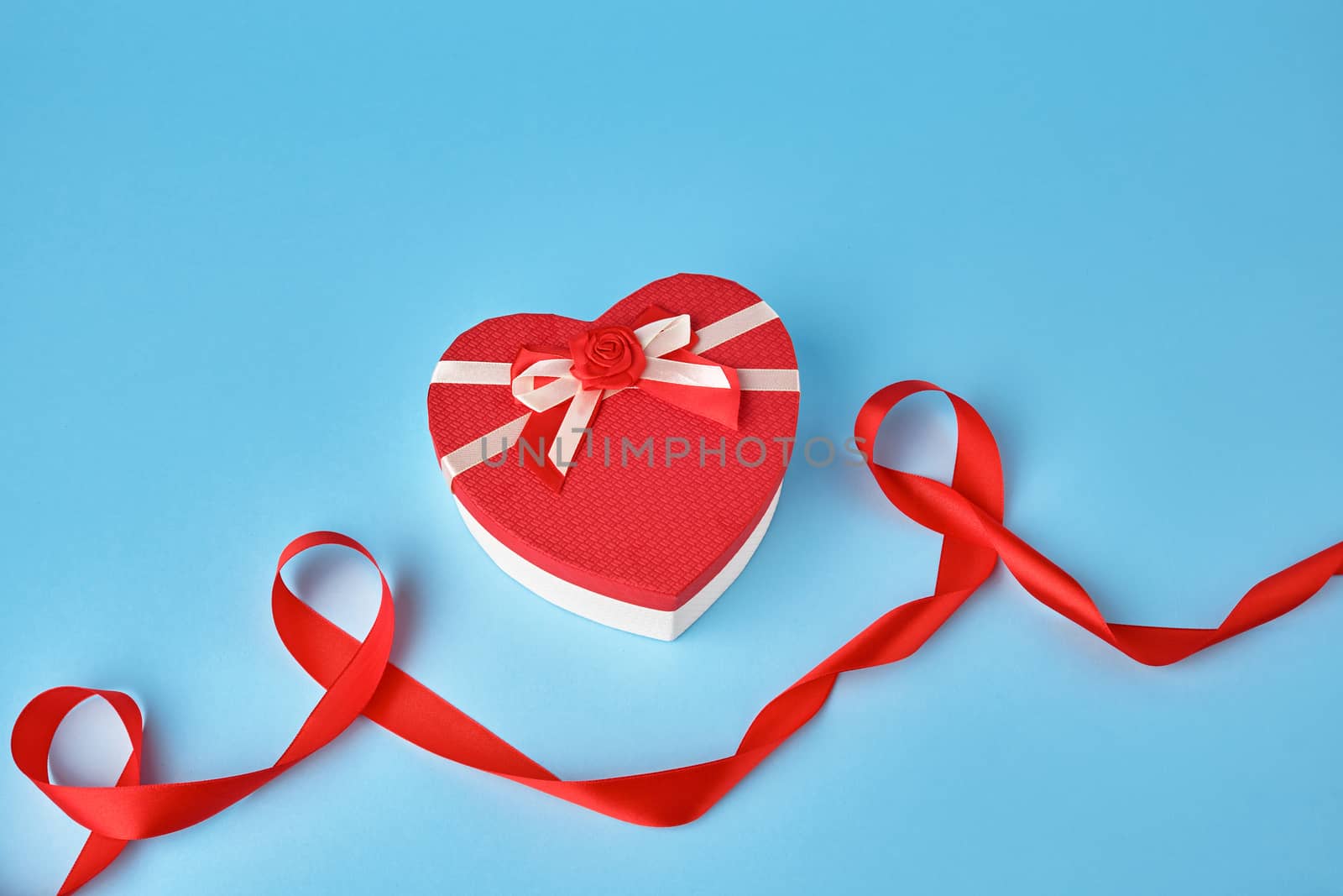 closed red heart-shaped gift box with a bow on a blue background, top view, festive backdrop. Valentine gift