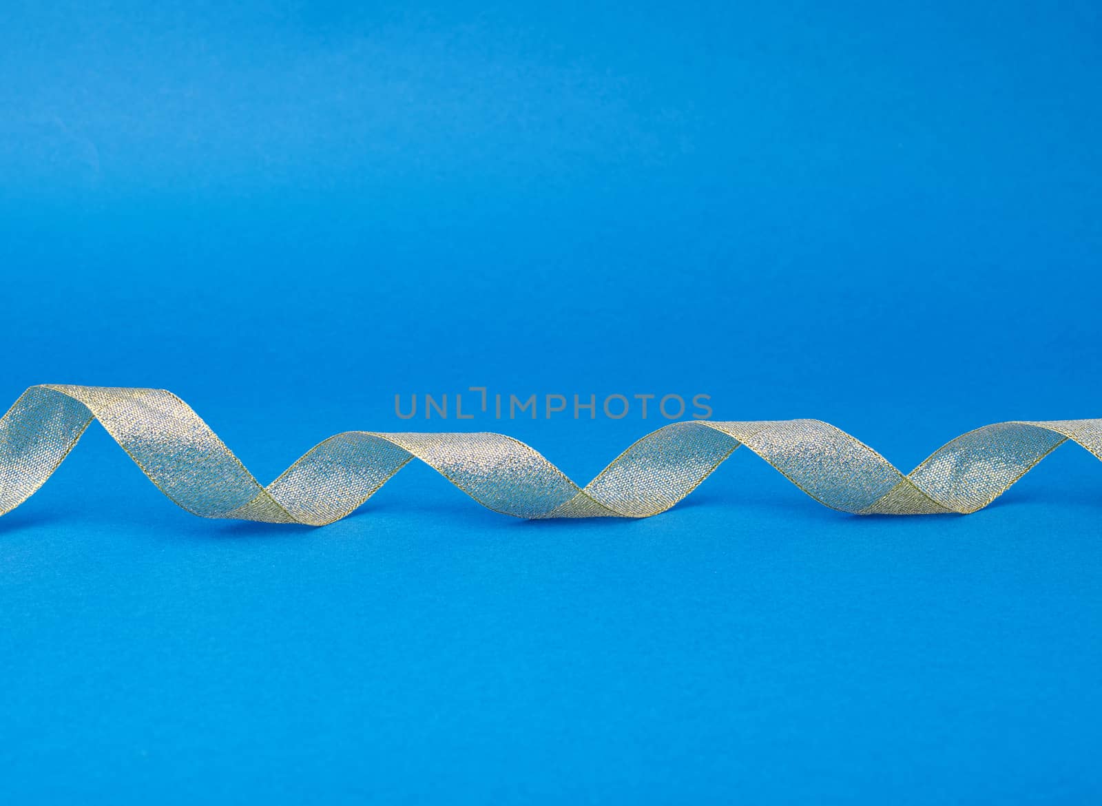 Shiny golden satin ribbon on a blue background. Beautiful banner for celebration design. Anniversary, birthday