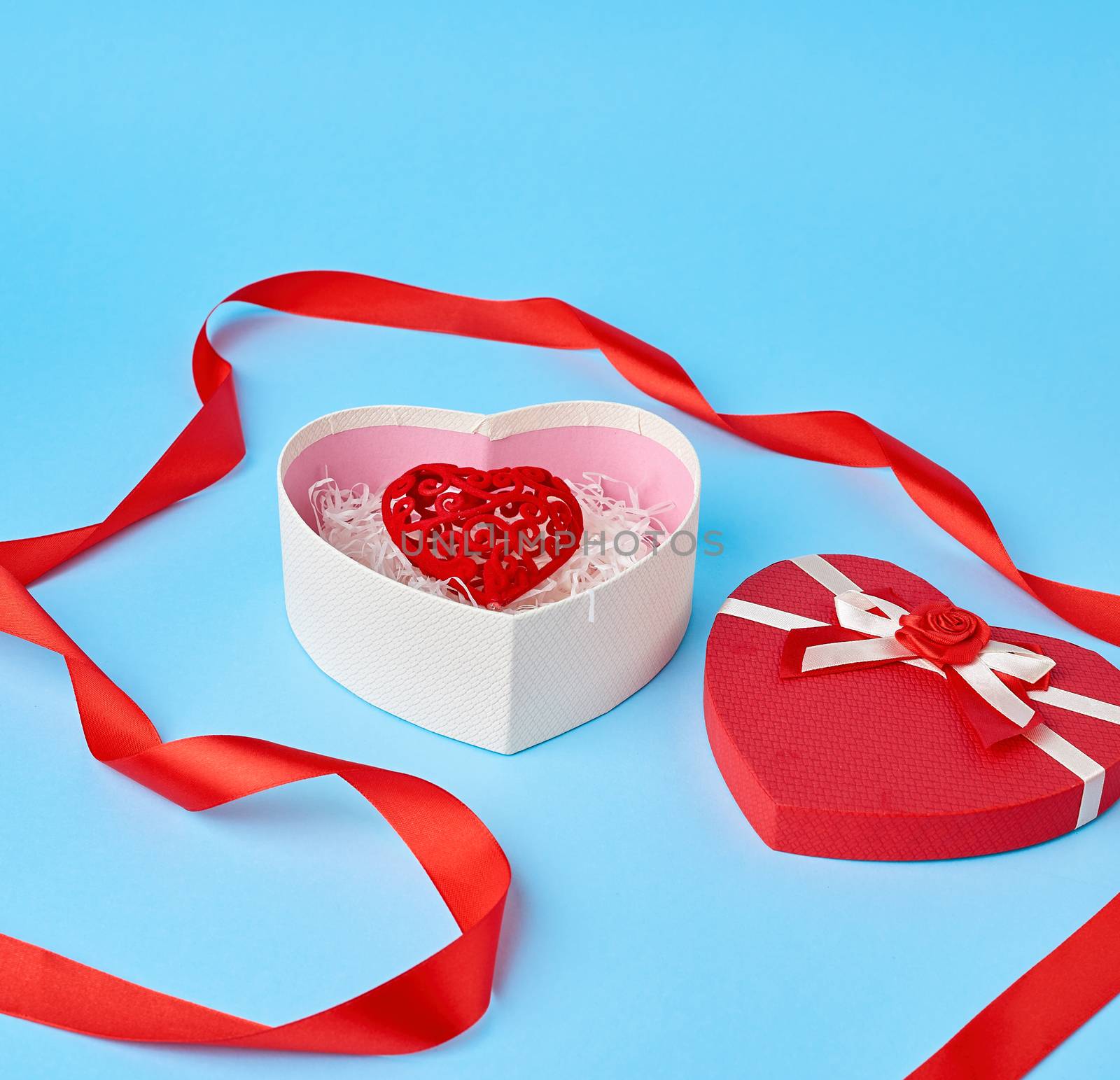open red heart-shaped gift box with a bow on a blue background, festive backdrop. Valentine gift