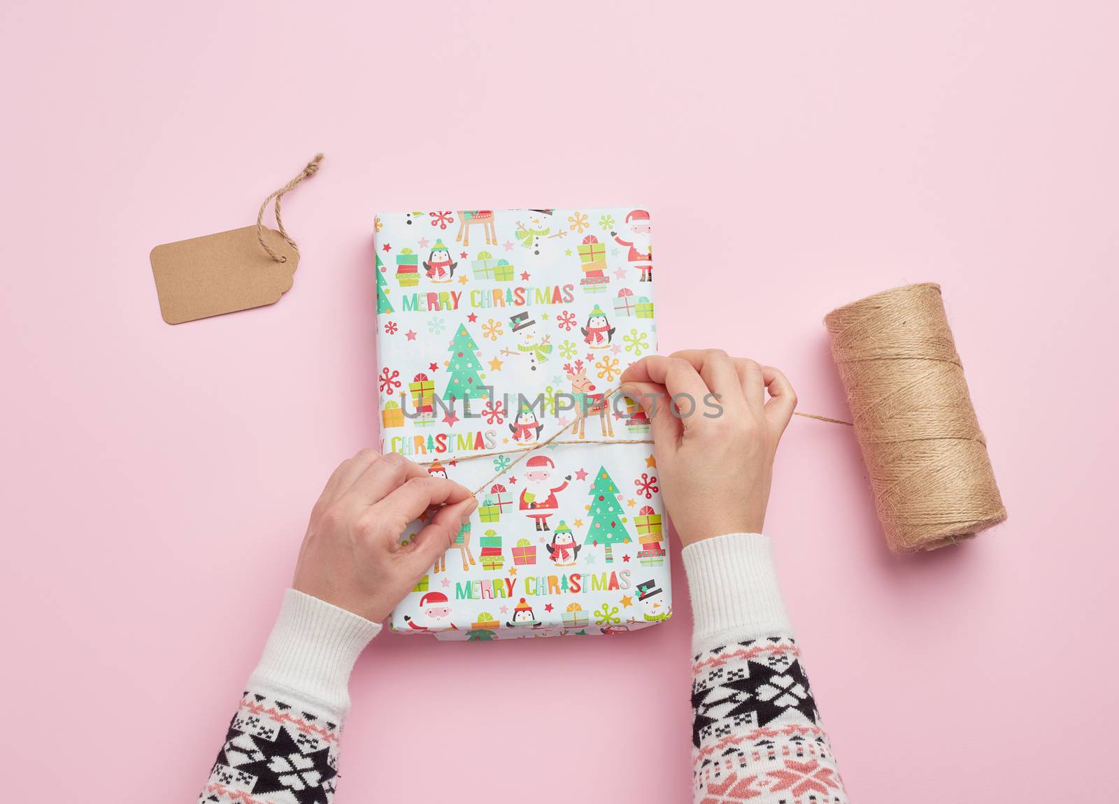 two female hands are wrapping a gift in holiday paper on a pink background, top view, do-it-yourself crafts, festive backdrop