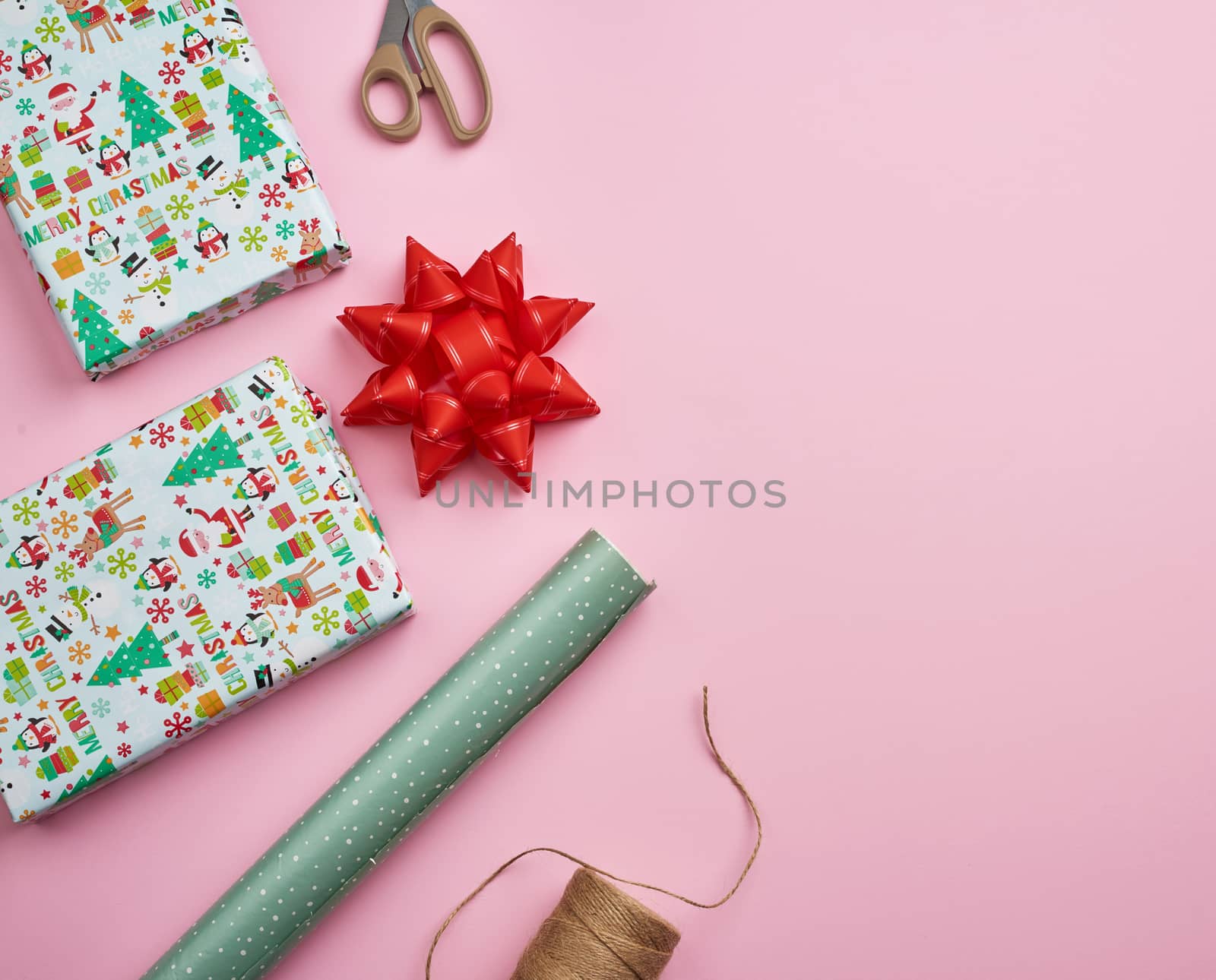 rolls with wrapping paper, brown rope, scissors, decor and a wrapped square box with a gift. DIY gift making process, pink background