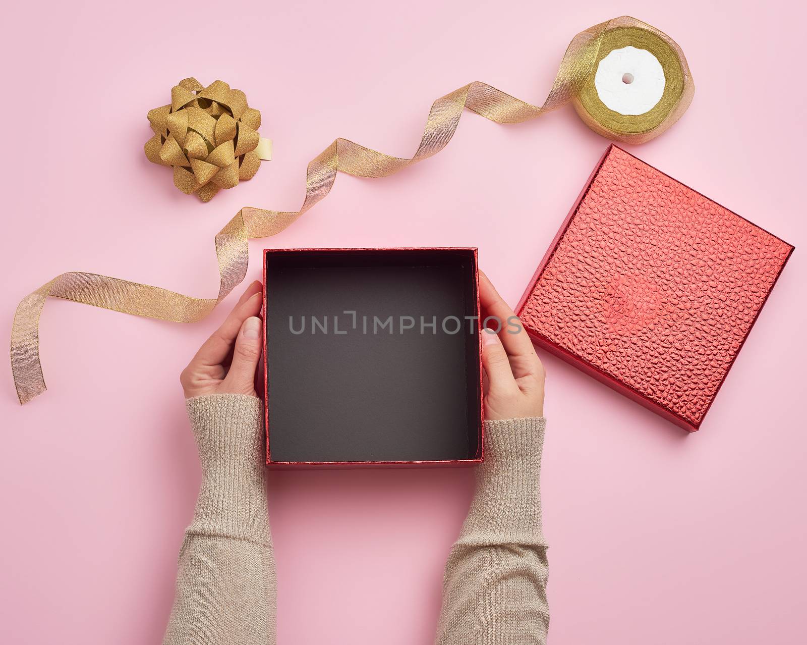 two female hands holding a square empty gift box over a pink background, top view